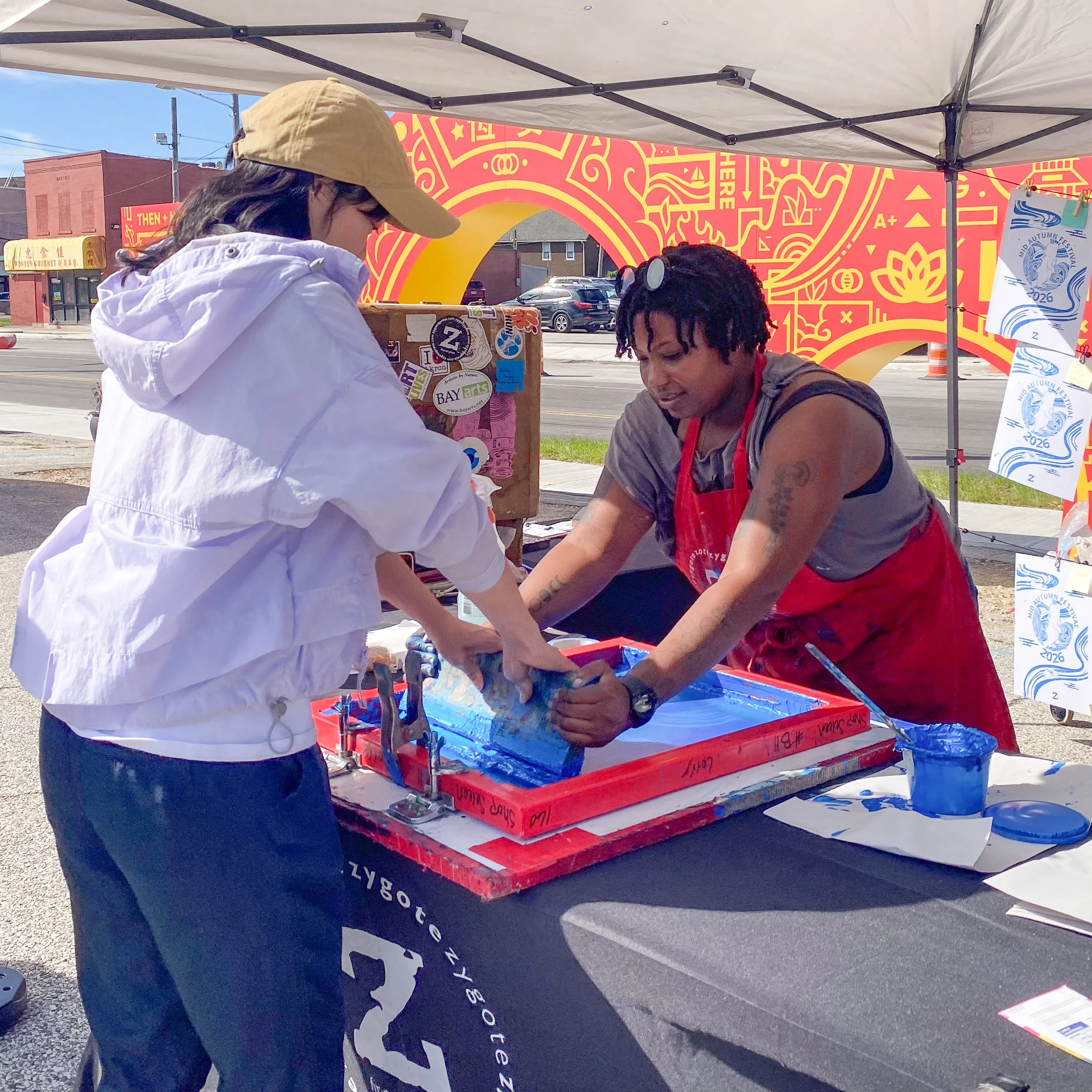 Community Engagement Manager Sequoia Bostick shows a young woman how to screenprint at the Mid Autumn festival