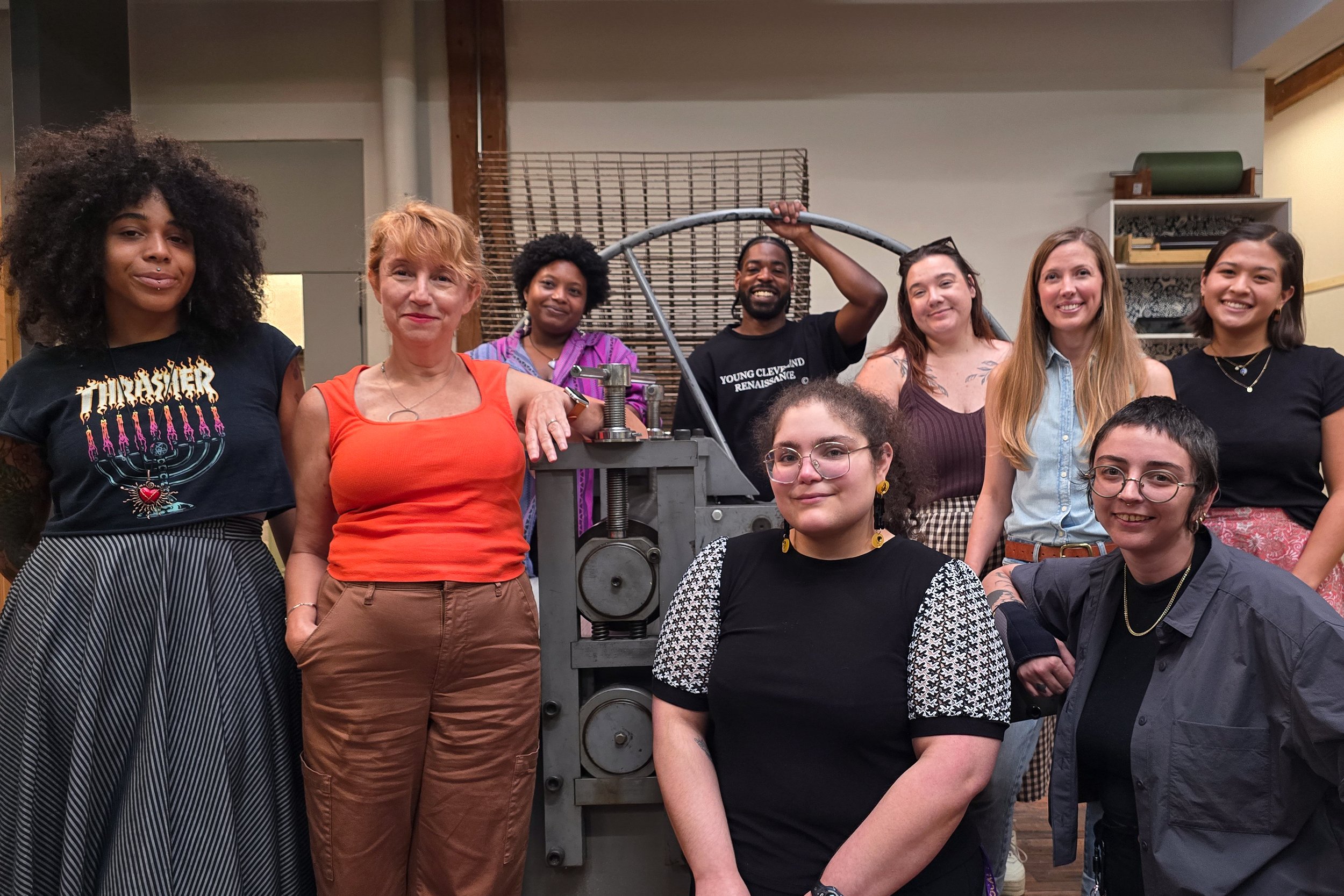 Group of diverse people posing in front of machinery in an industrial or workshop setting.
