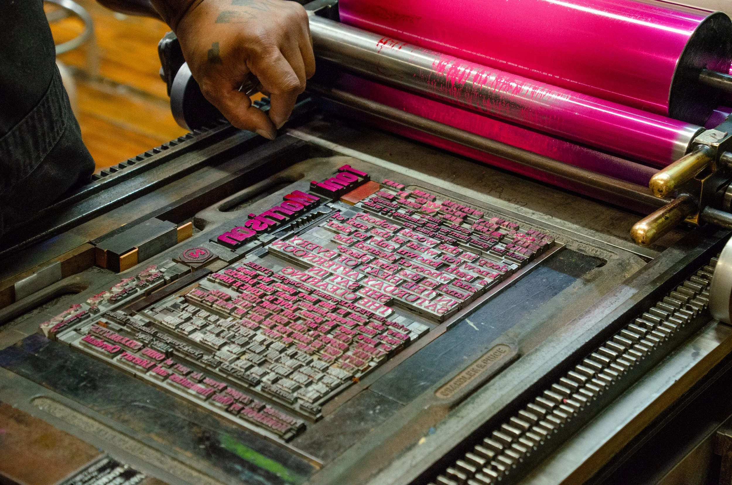 Person rolls bright pink ink onto a letterpress set with metal type.
