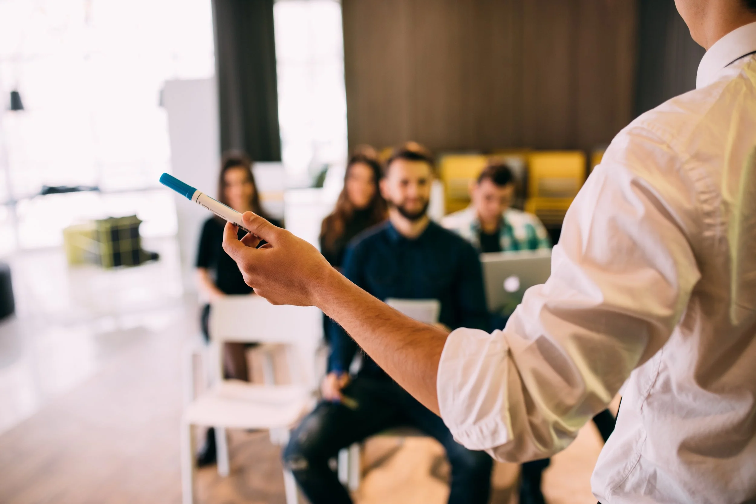 Person holding a whiteboard marker in front of a seated audience during a presentation or workshop.
