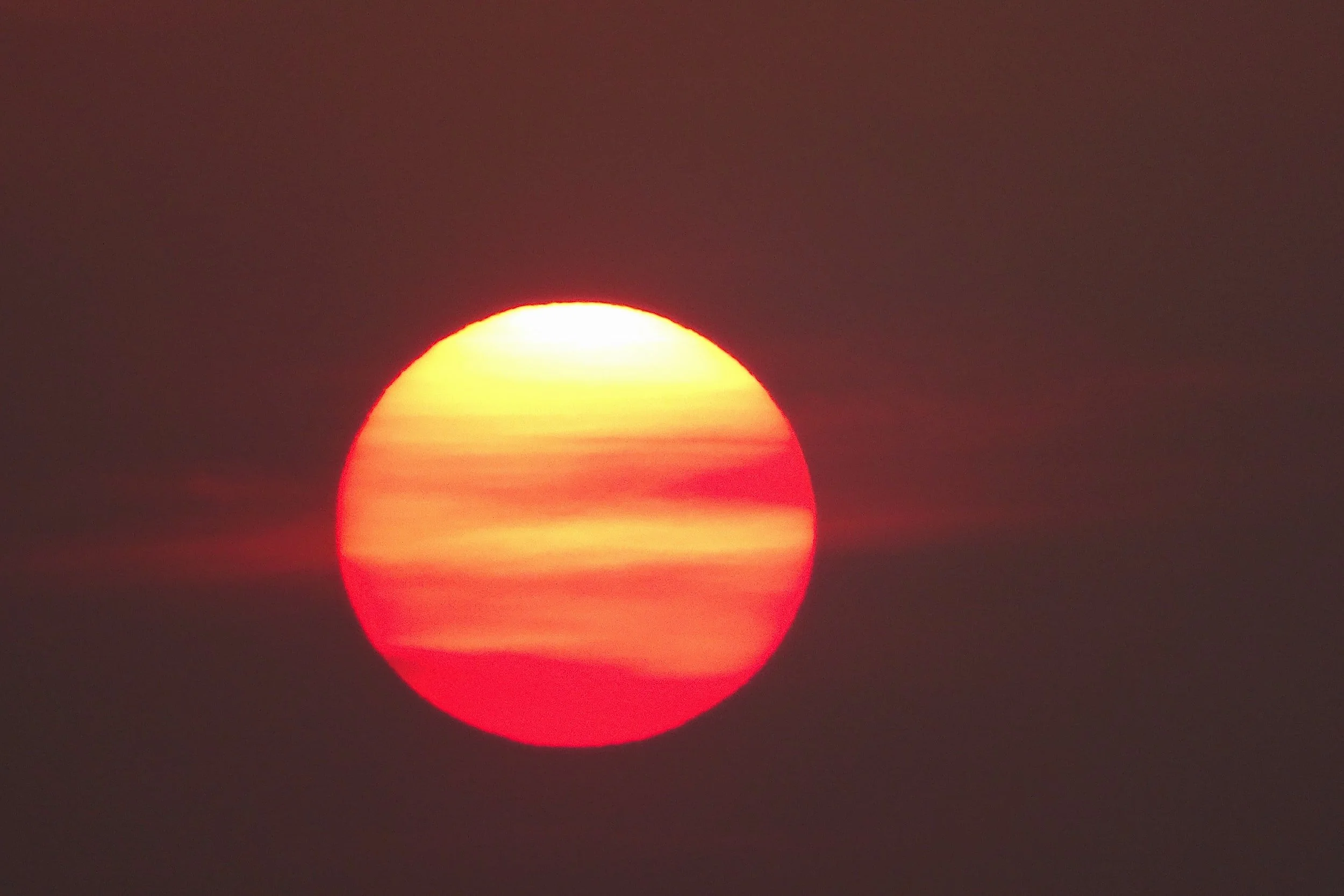 A vibrant sunset with the sun partially obscured by clouds, creating a reddish-orange glow in the sky.