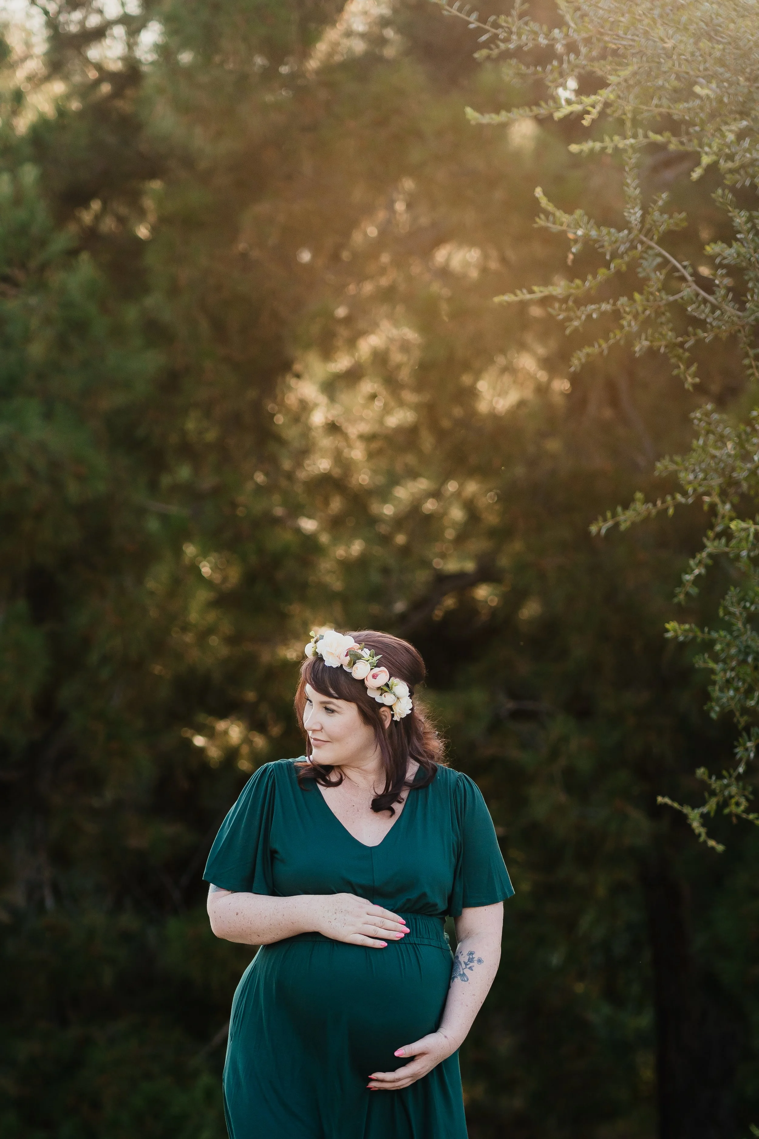 pregnant woman in a green dress holding belly in a forest
