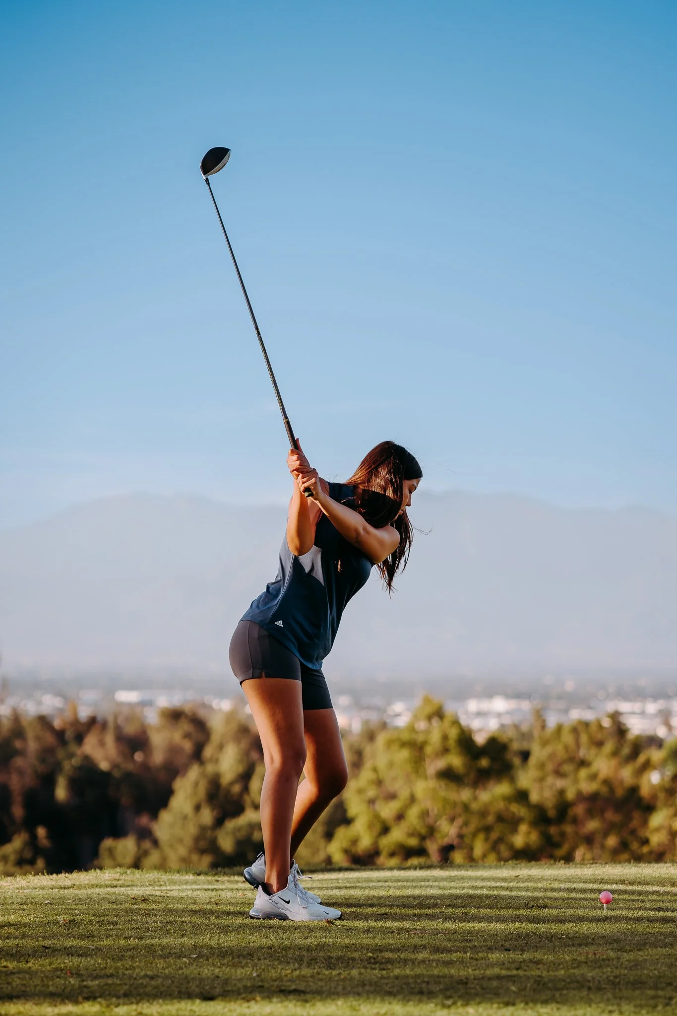 Teenager teen girl at golf course swinging golf club driver pink golf ball on a tee