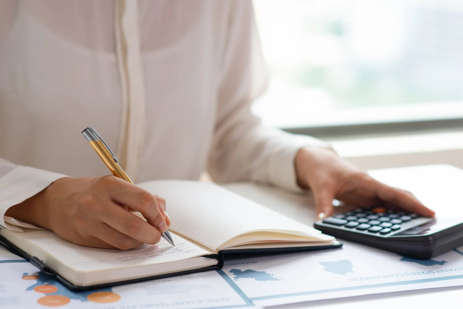 a lady writing on a notebook with a calculator beside the notebook