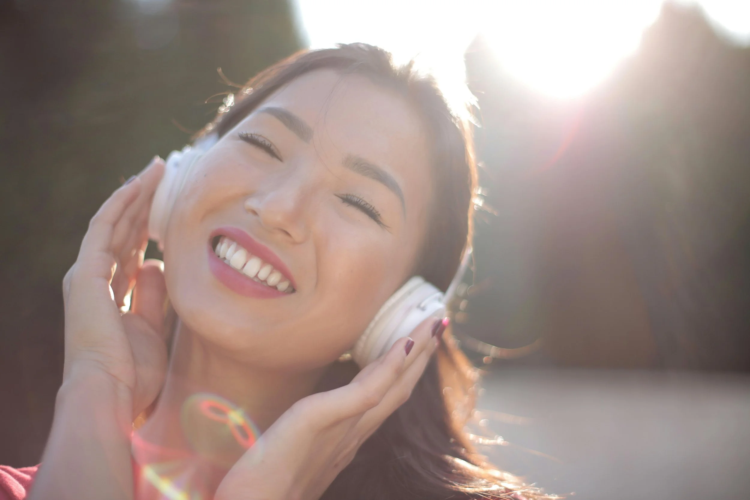 A calm hopeful woman shown in natural light listening to something on her headphones and showing signs of relief after QCore treatment.