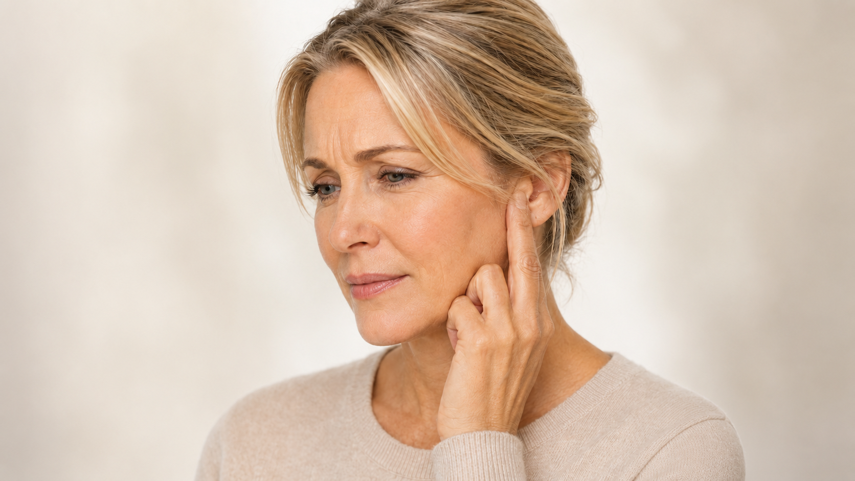 Woman holding finger to ear with a troubled look on her face who appears to be struggling with the constant sounds of tinnitus.