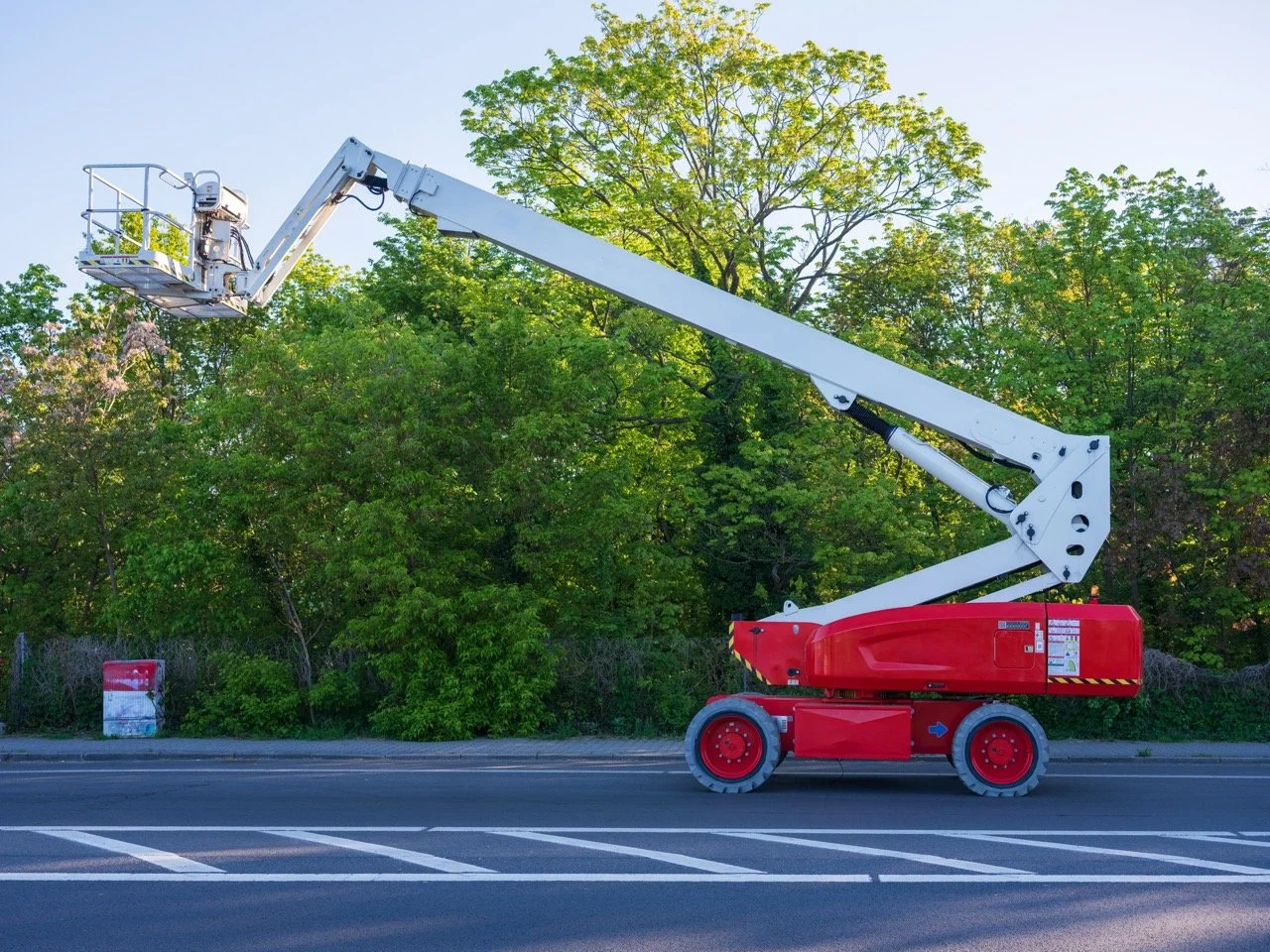 Articulating boom lift extended outdoors with its work platform raised beside trees