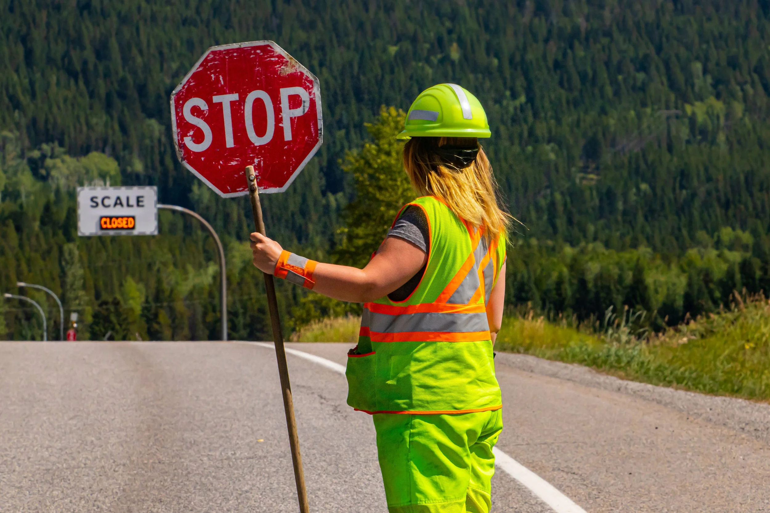 Traffic control worker in high-visibility clothing holding a stop sign on a roadway