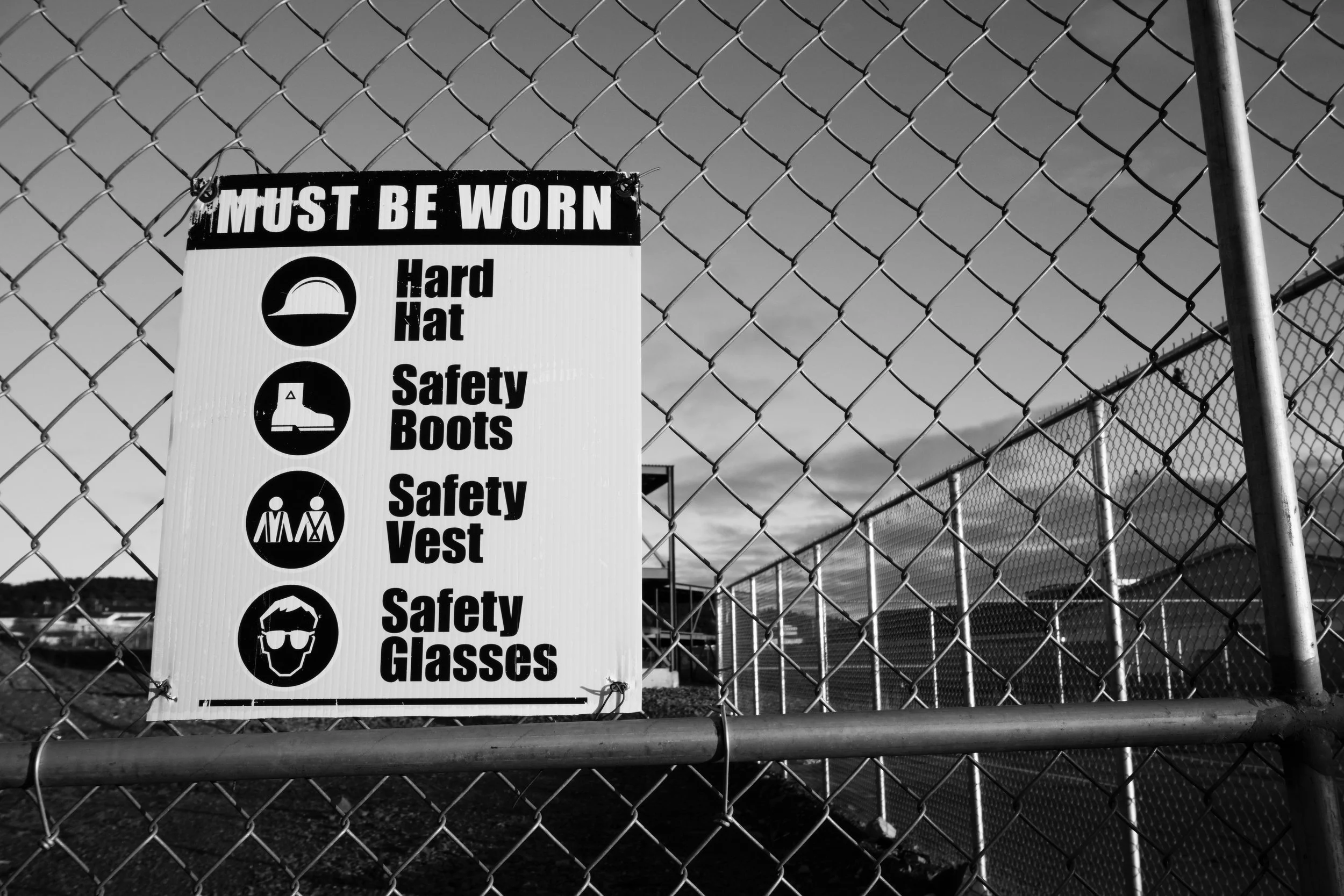 Construction site sign listing required hard hat, safety boots, safety vest, and safety glasses