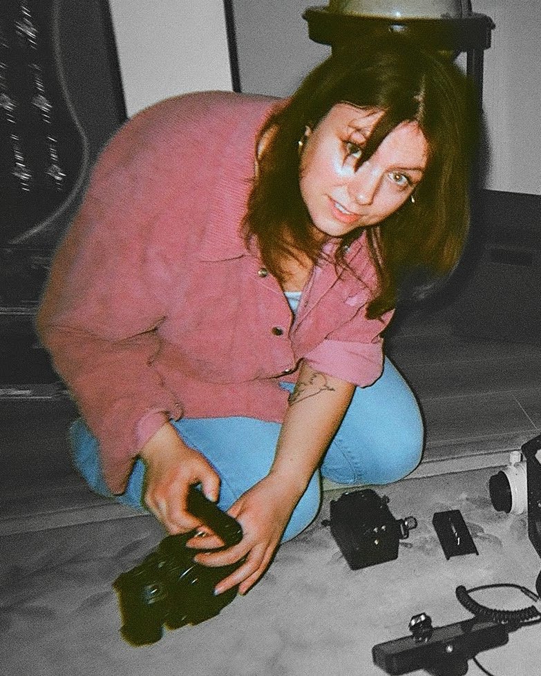 Woman kneeling on the floor holding a handgun, surrounded by firearms and gun accessories.