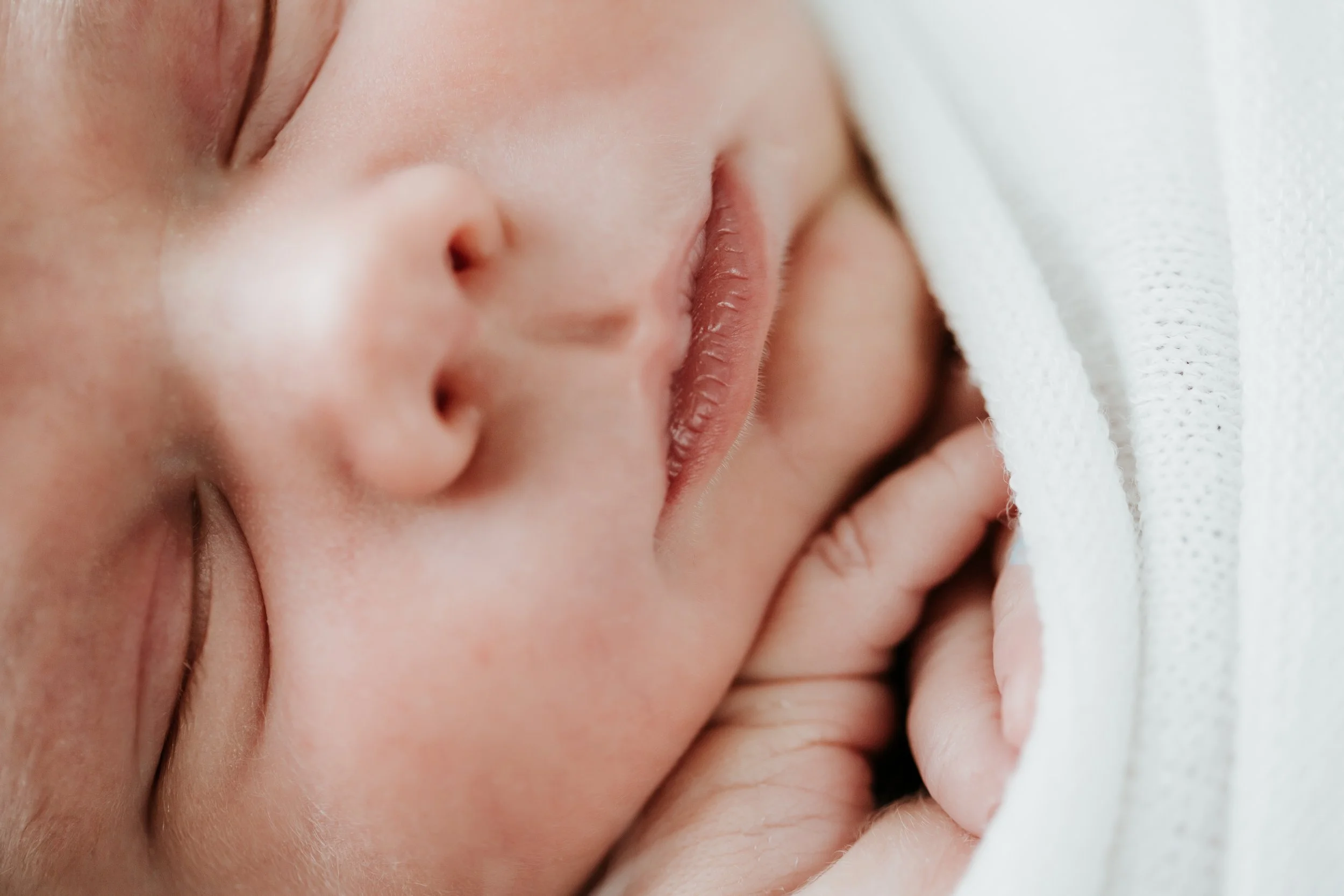 Close-up image of a sleeping baby's face with peaceful expression, lying on a soft surface.