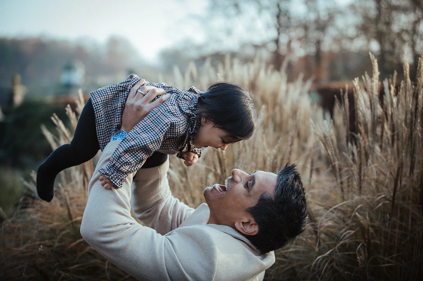 A man holding a young girl in the air in a field of tall, golden grass during sunset.