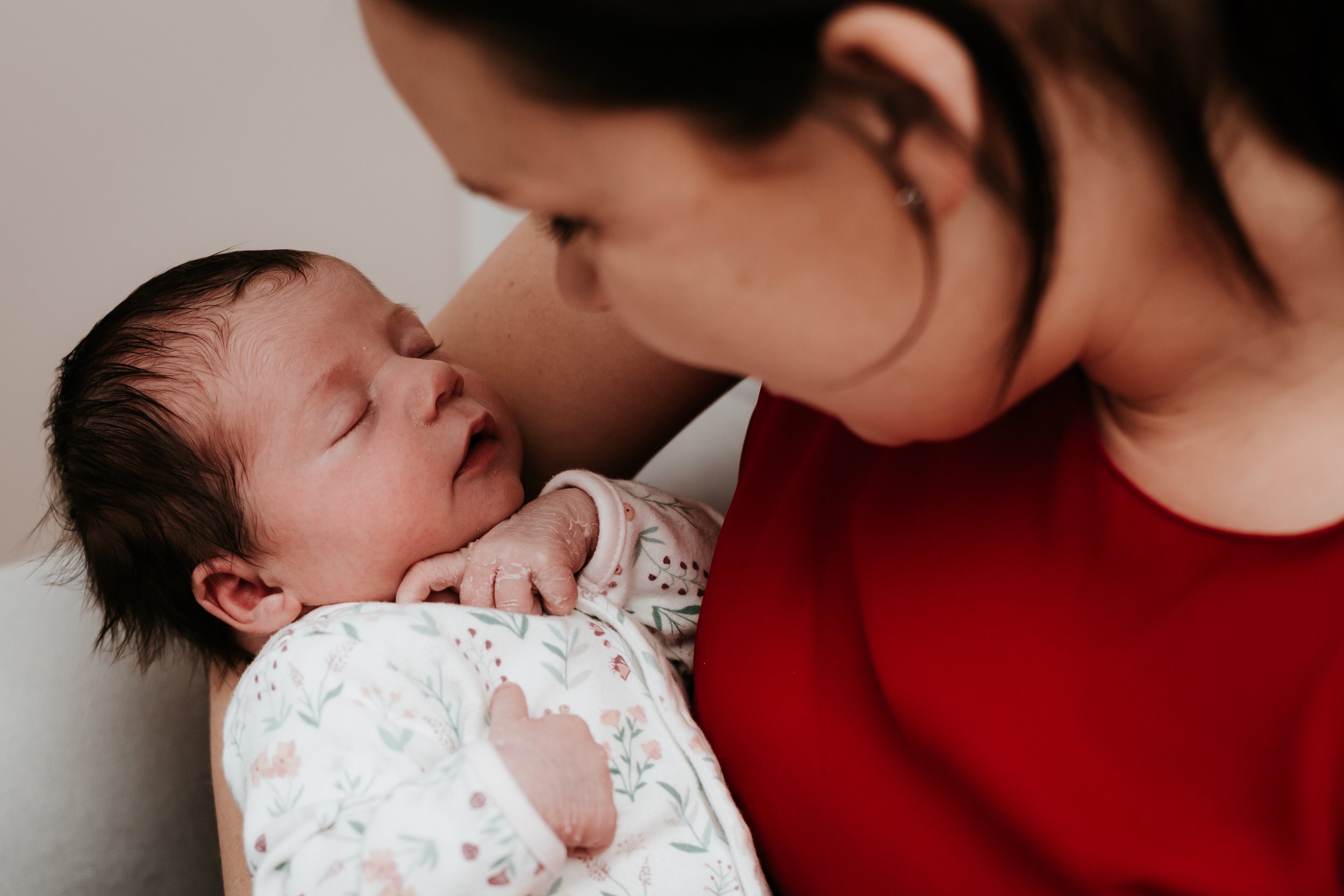 A woman is holding a newborn baby close, both with eyes closed, sharing an intimate moment.
