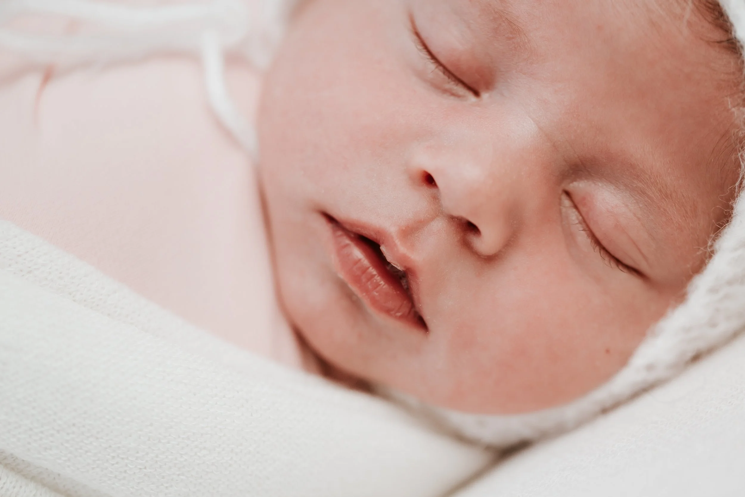 Close-up of a sleeping baby with a peaceful expression, lying on a soft white surface.