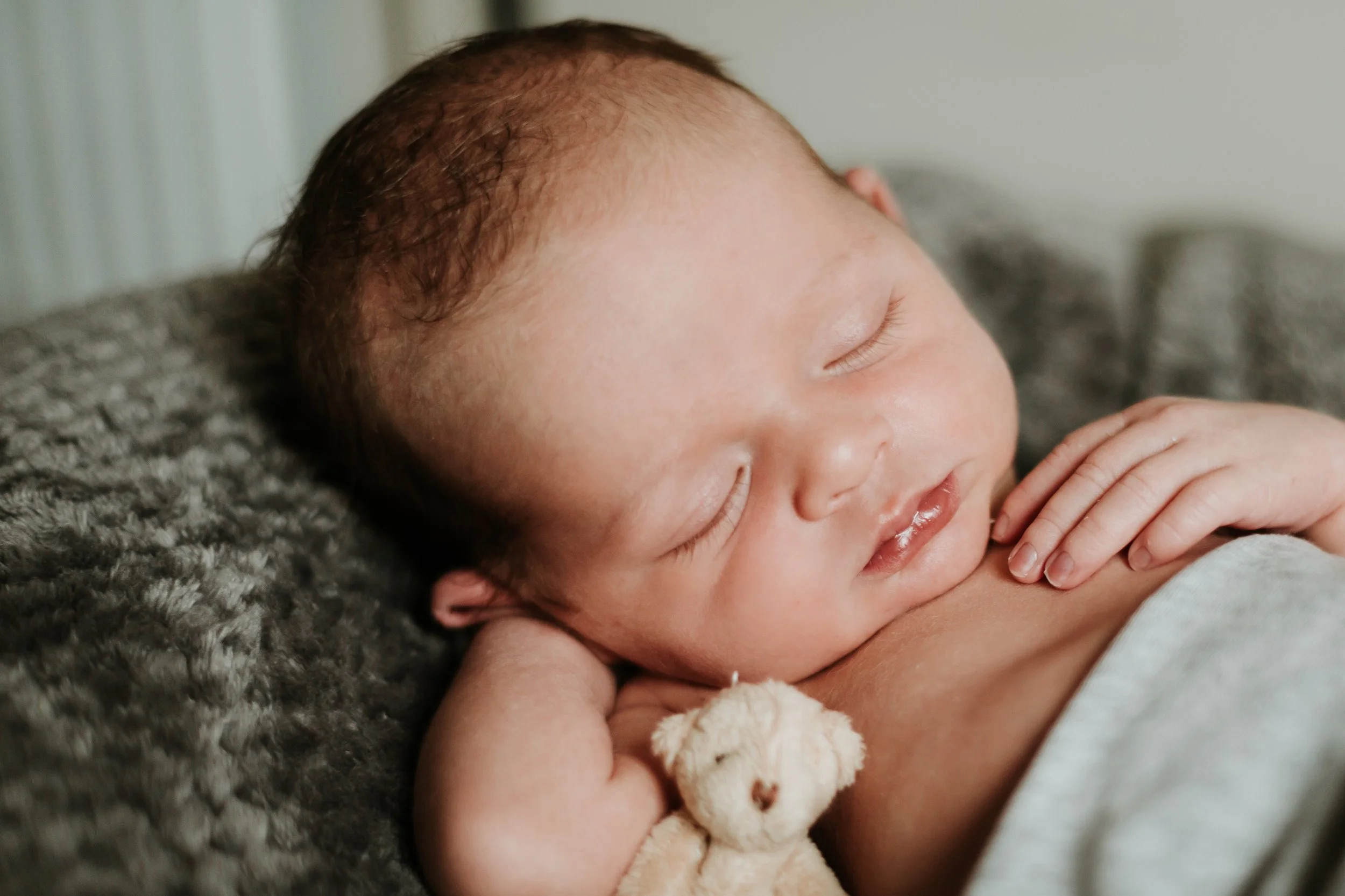 A sleeping newborn baby resting on a soft blanket, holding a small stuffed toy.