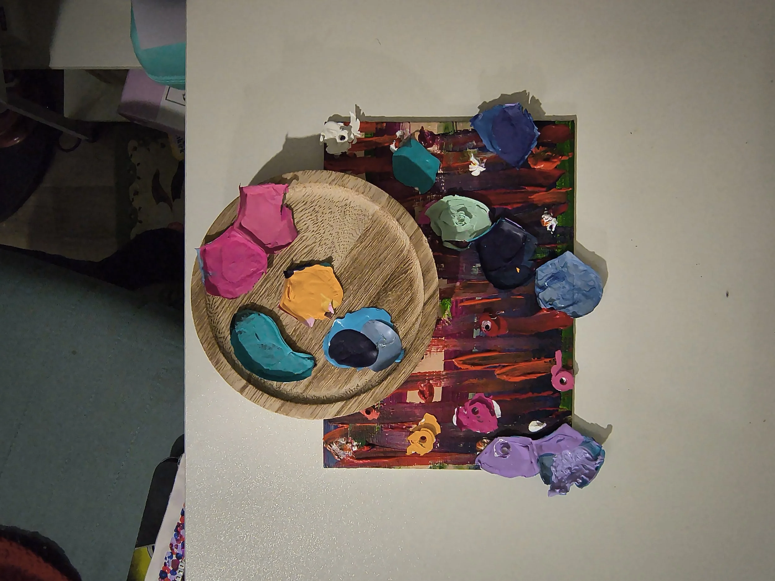 Colorful crumpled paper pieces on a round wooden plate and a painted canvas background.