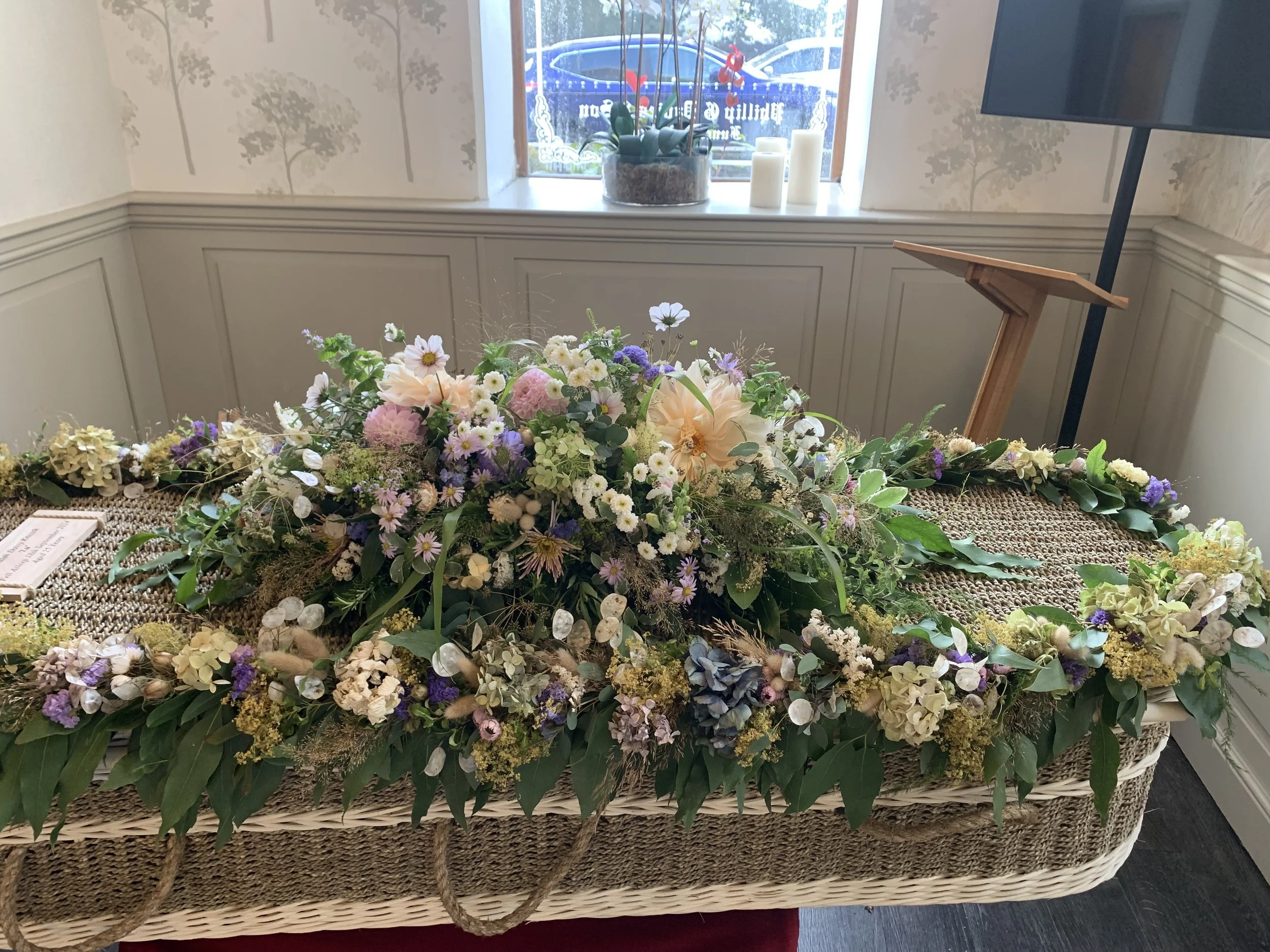 Natural funeral flower tribute with peach dahlias and white cosmos on a woven coffin from Blue Hill Flora