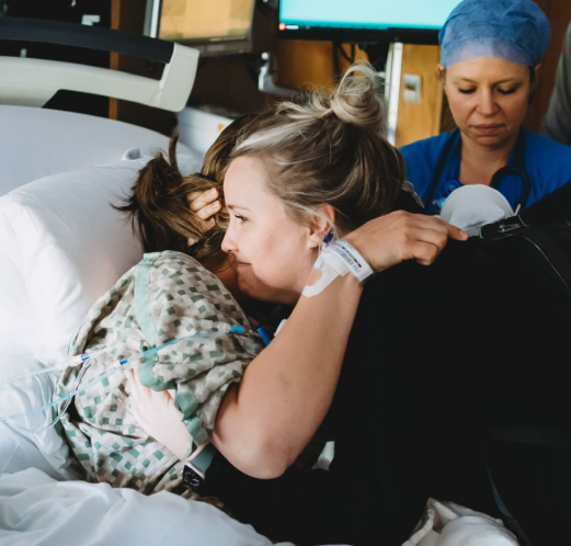 A woman in a hospital bed hugging a young girl, with a nurse nearby.