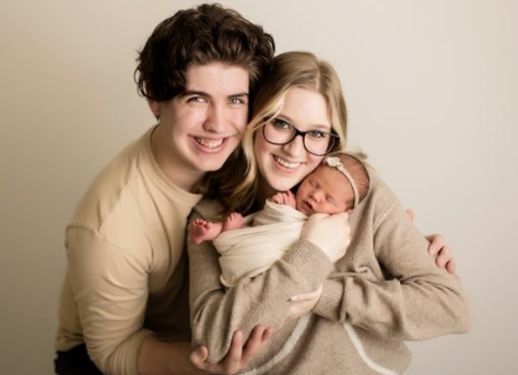 A happy family with a woman holding a newborn baby, a young man and woman smiling together against a neutral background.