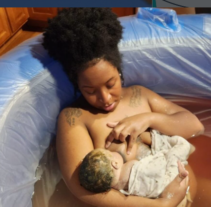 A woman with natural hair holding a newborn baby in a hospital setting.