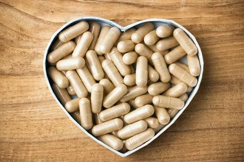 Heart-shaped container filled with beige capsules on a wooden surface.
