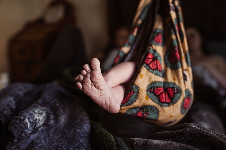 A child's bare foot sticking out from under a blanket with colorful butterfly patterns, on a bed in a cozy bedroom.