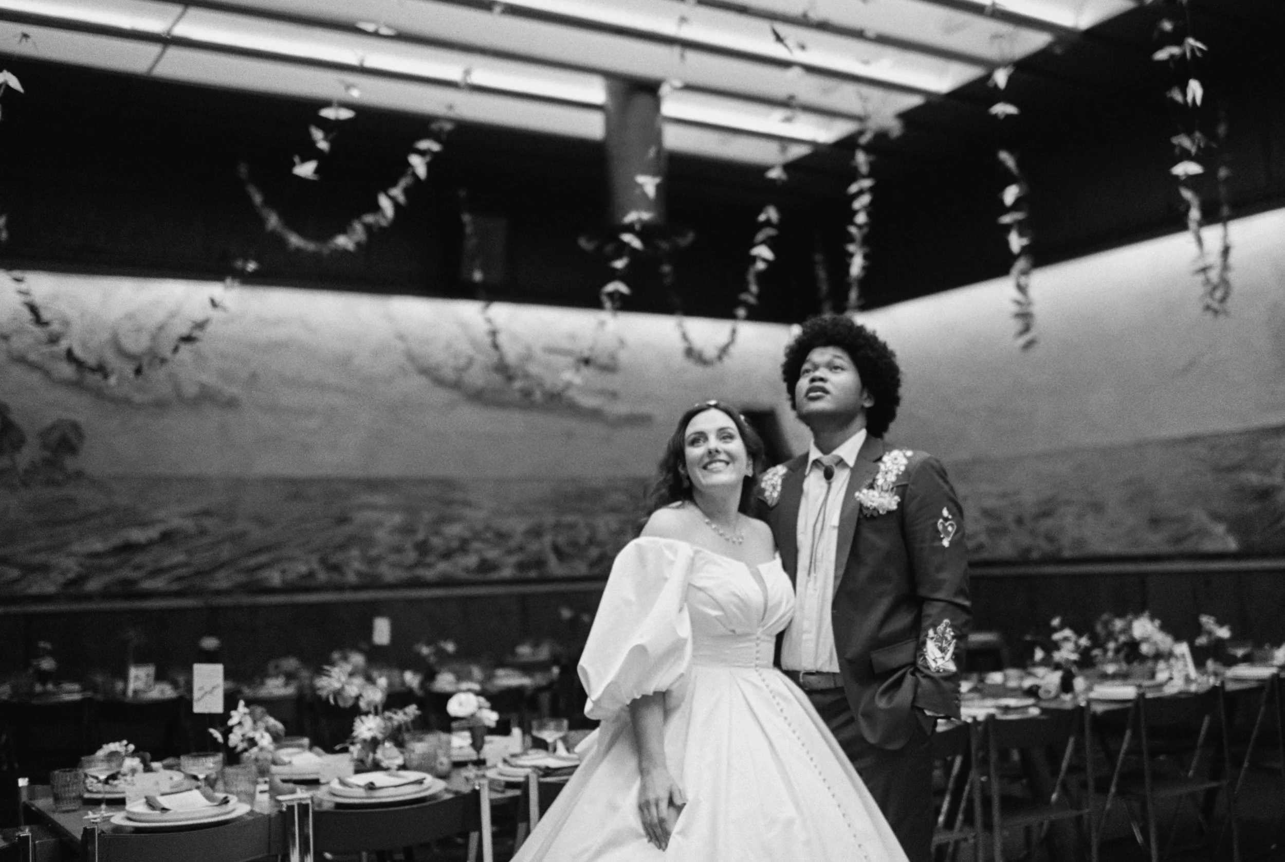 A bride and groom standing together at their wedding reception in a decorated venue, smiling and looking in different directions.