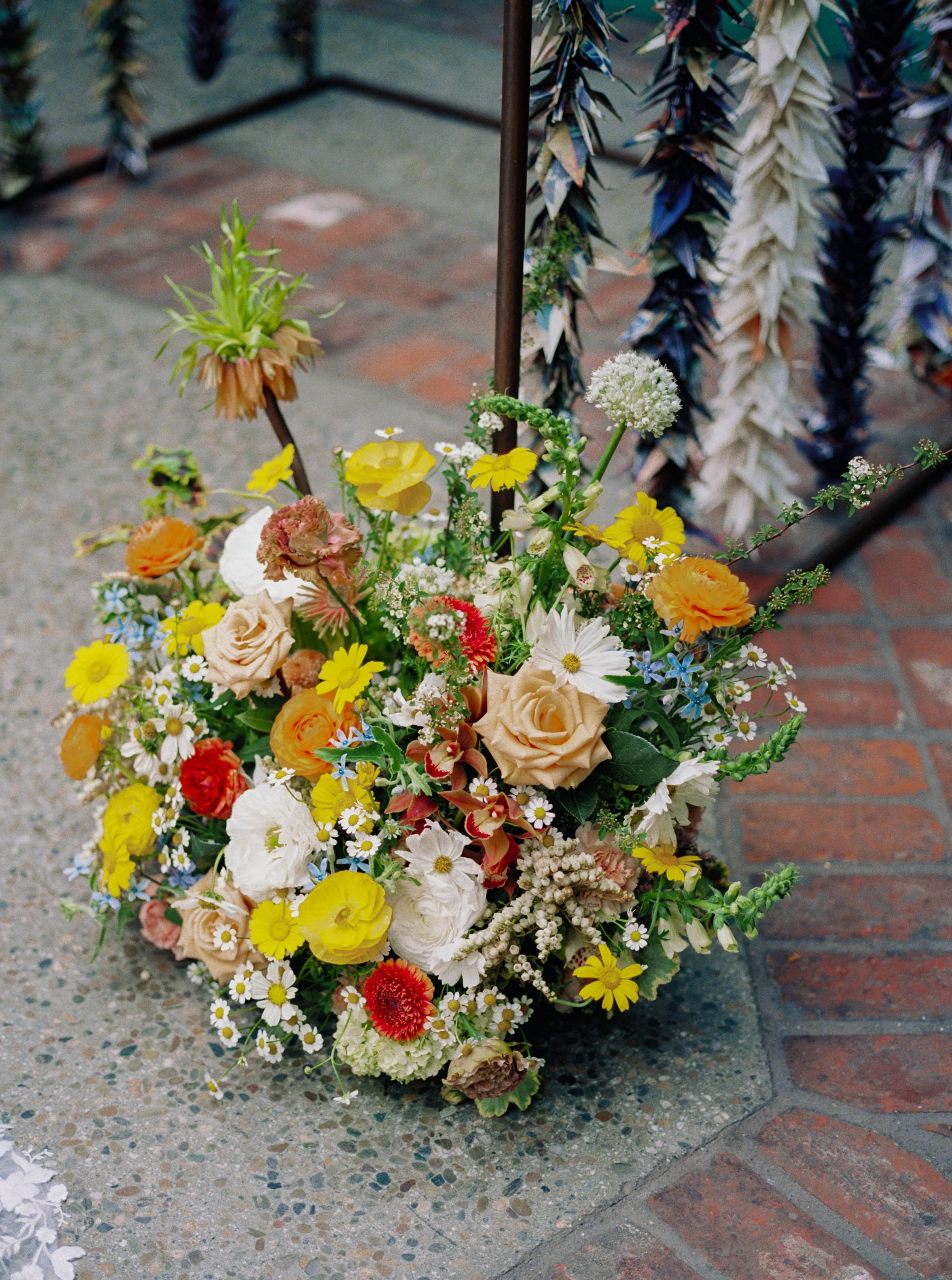 A colorful bouquet of mixed flowers, including roses, daisies, and filler flowers, placed in front of a Jewish wedding chuppah.