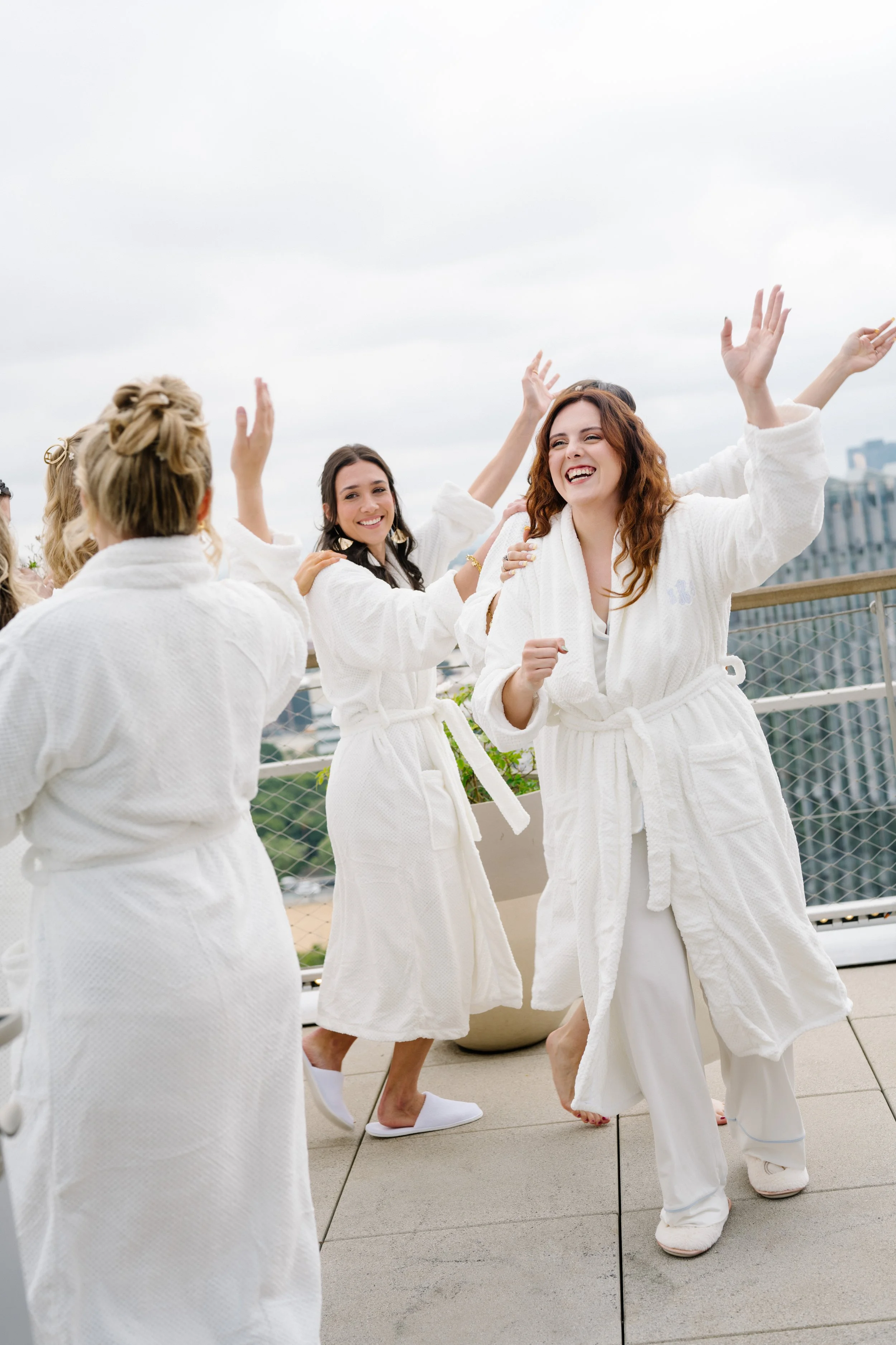 Group of women in white robes celebrating on a rooftop terrace.