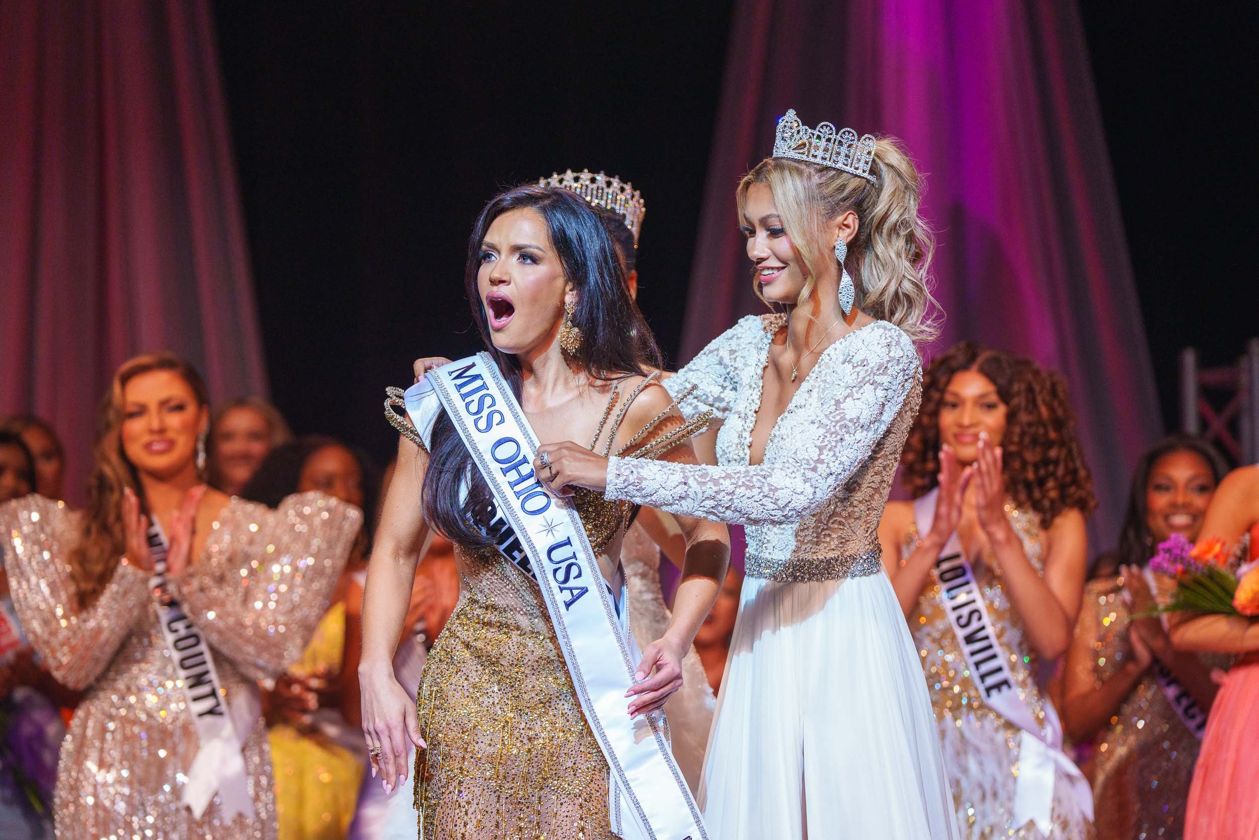 Miss Ohio2025 pageant winner being crowned and sashed on stage, surrounded by contestants clapping.