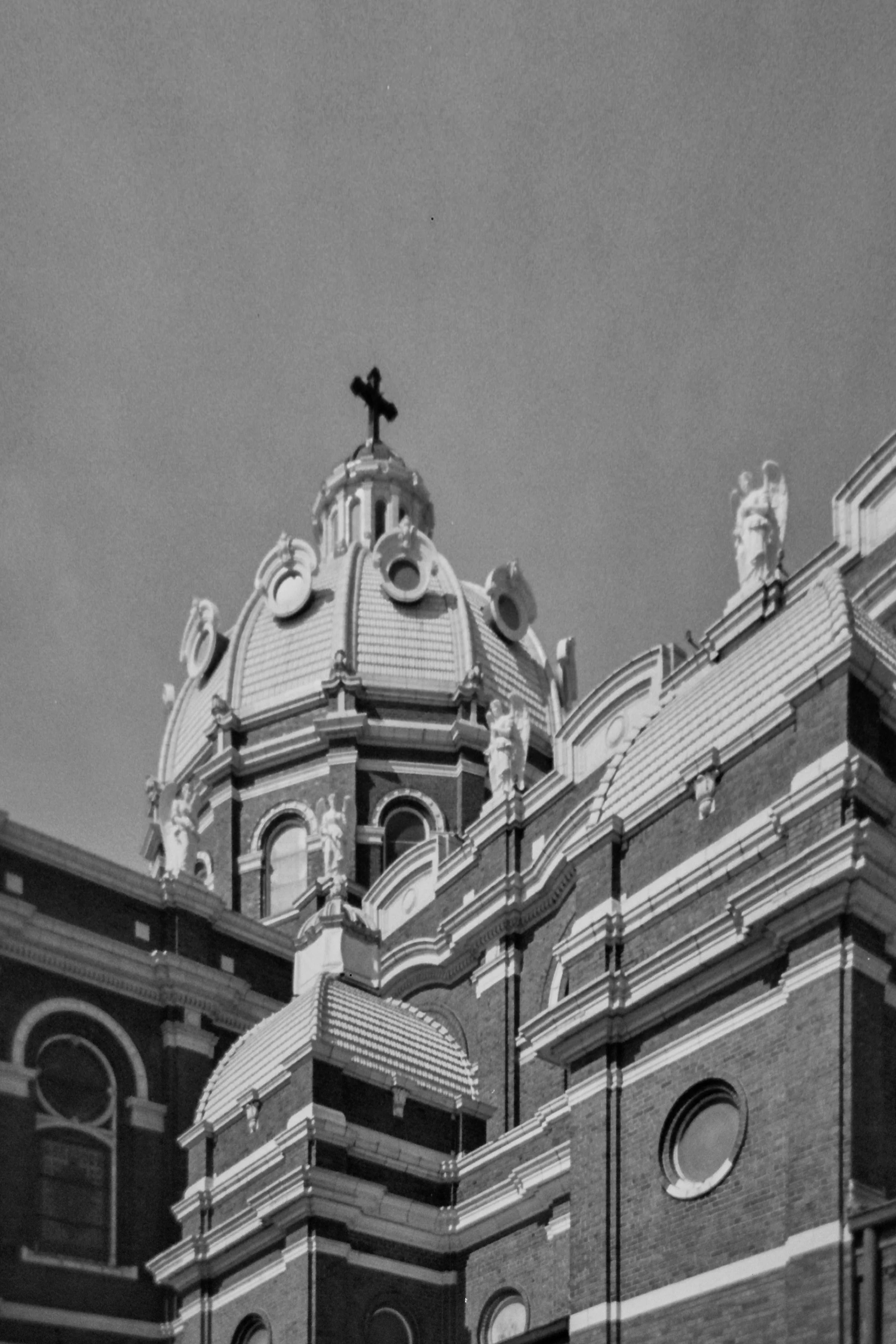 Black and white photo of a historic building with ornate architecture, a domed roof with a cross on top, and statues along the roofline.