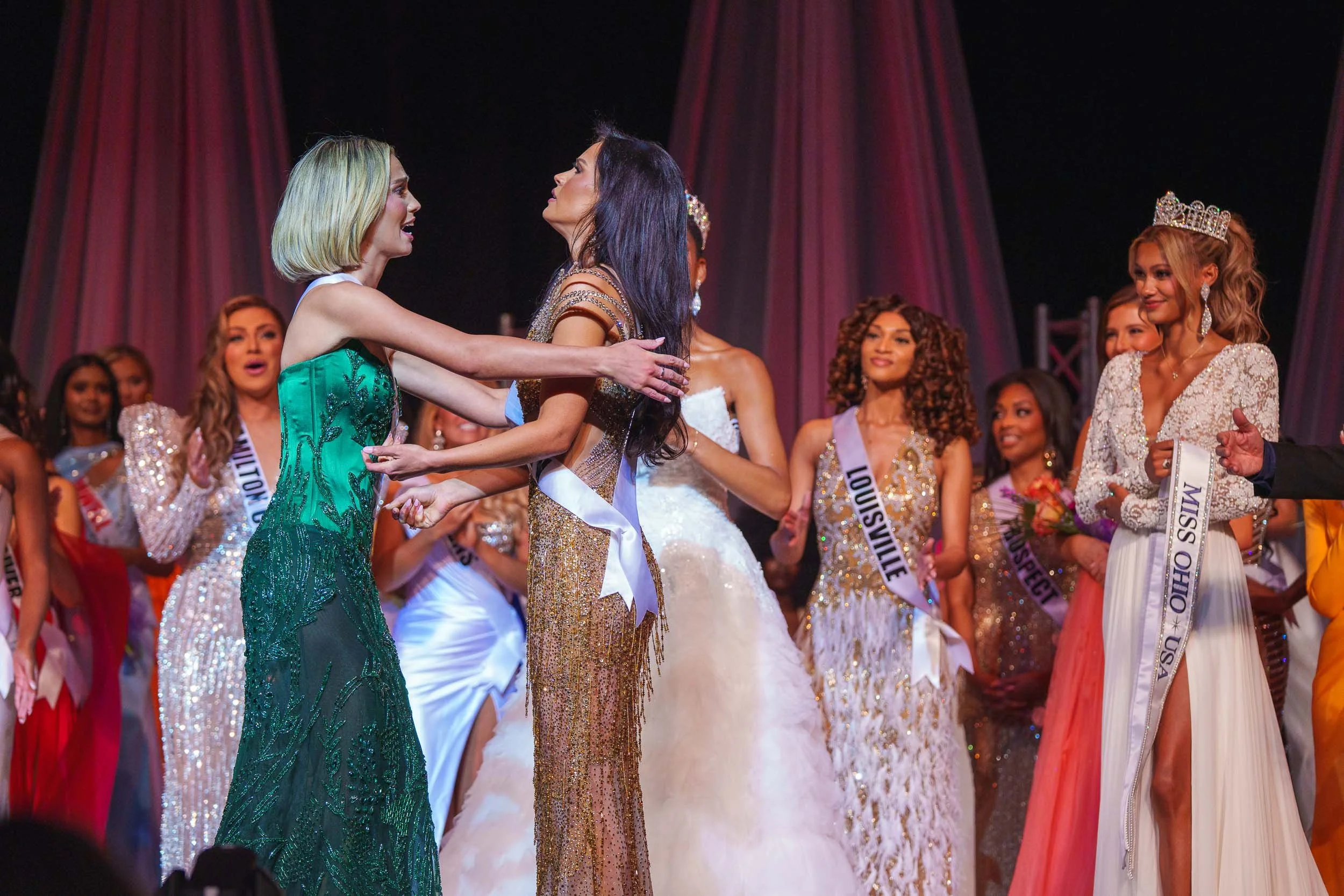 Miss Ohio 2025 final two contestants hugging on stage with other contestants in the background.