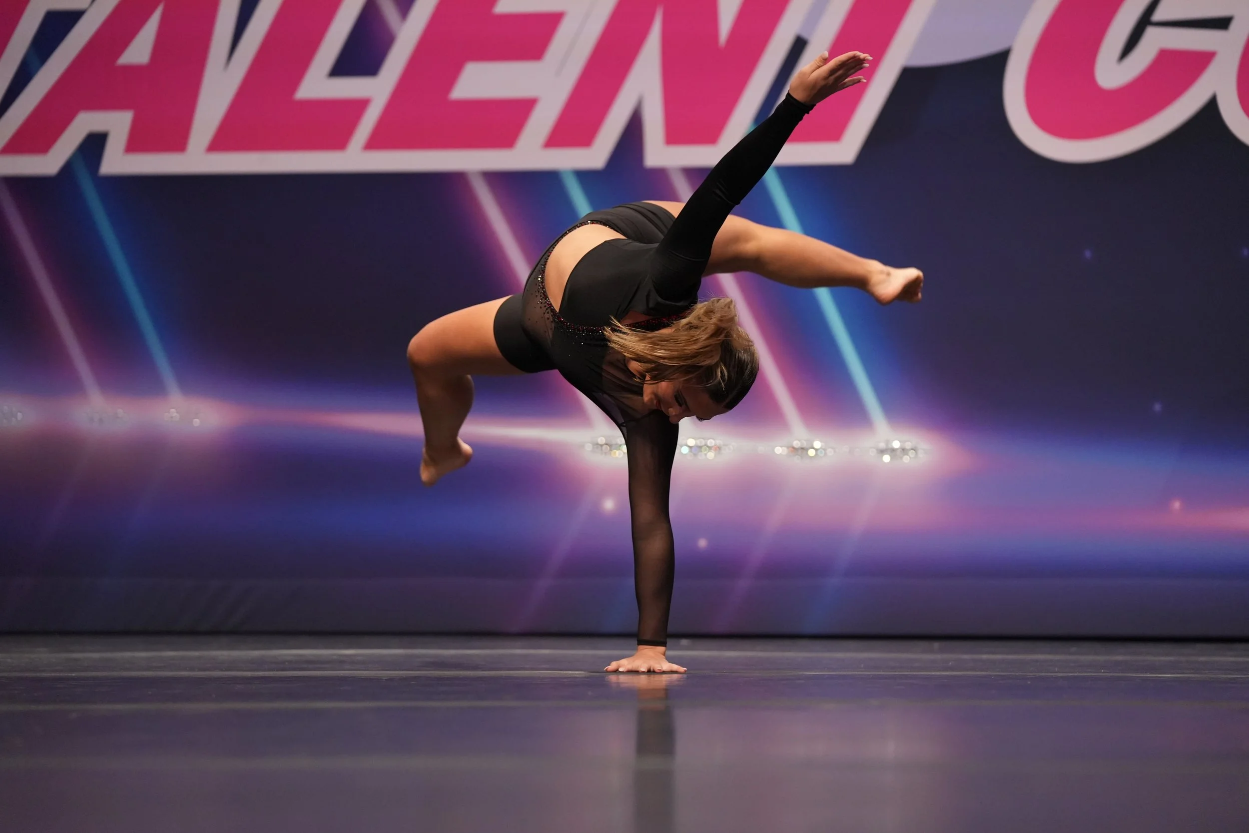 A woman performing a one-handed handstand on stage during a dance or gymnastics competition.