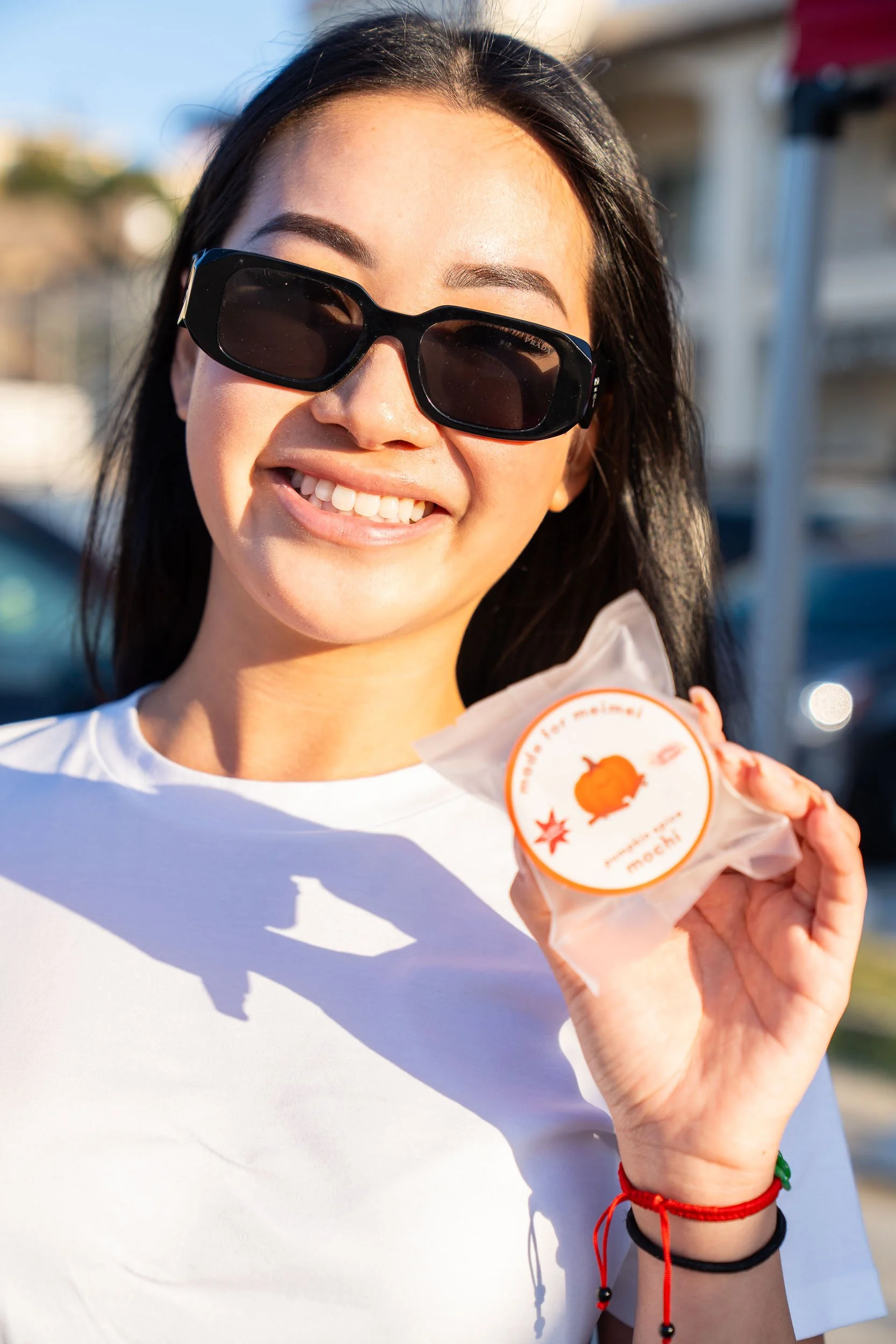 Smiling young woman wearing sunglasses holding a packaged mochi in an outdoor setting