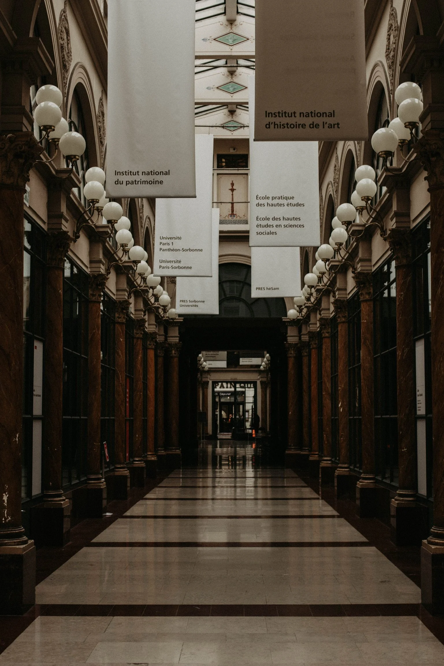 Interior of a historic building with high arched ceilings, marble columns, and hanging banners with French inscriptions.