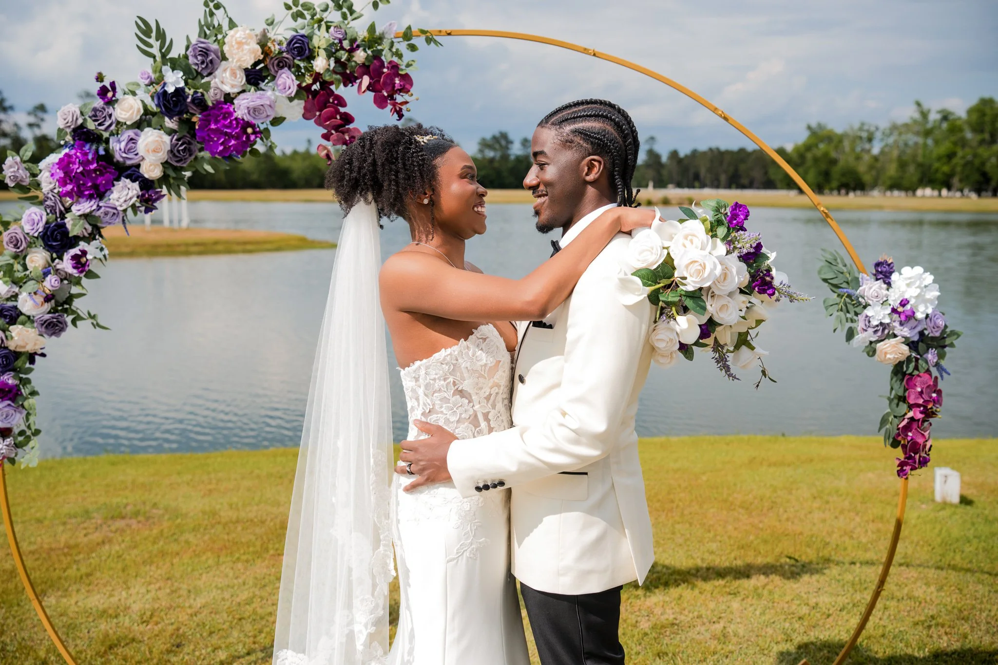 Bride and groom laughing under purple floral arch at Chateau 1800 lakefront wedding venue in Rincon GA near Savannah captured by Johannas J Photography