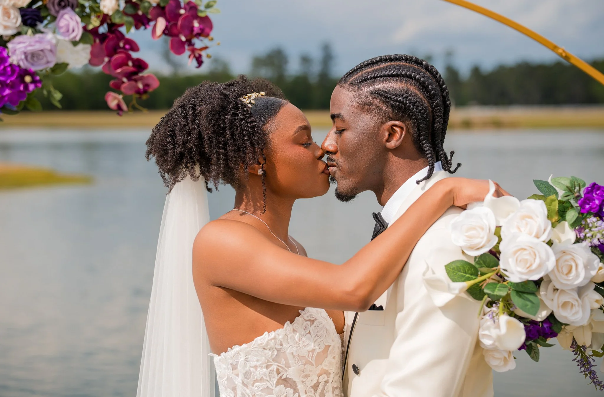 Bride and groom sharing first kiss under floral arch at Chateau 1800 lakefront wedding venue in Rincon GA near Savannah captured by Johannas J Photography