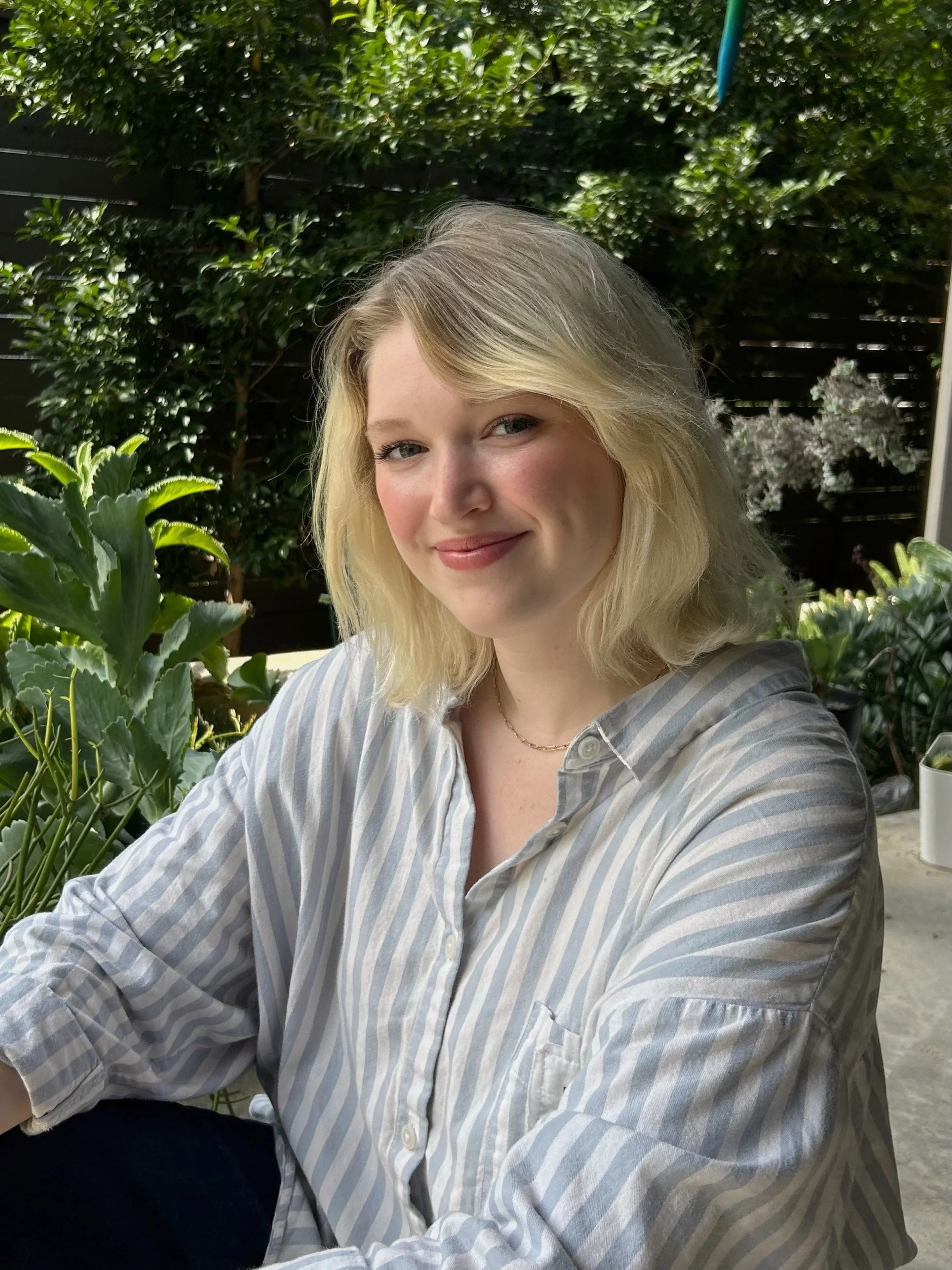Headshot of Hallie Hasenbank sitting on outdoor steps in front of plants.