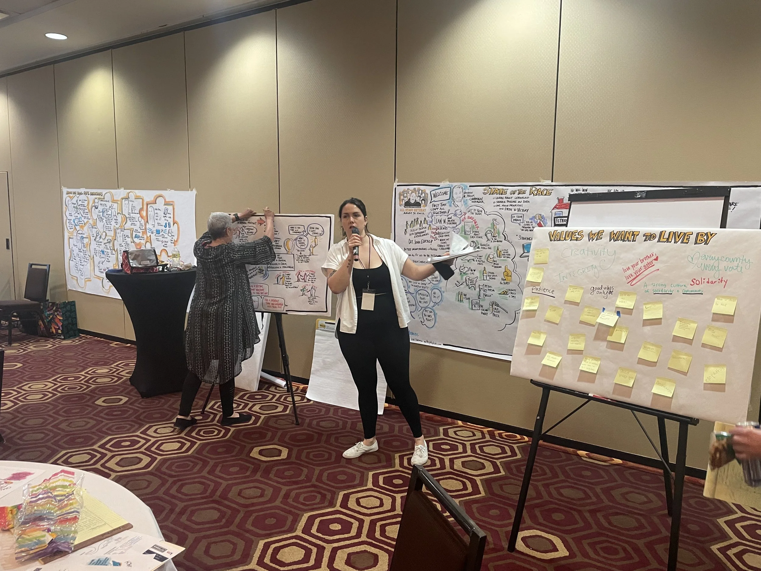 Kinship coach, Jules, facilitates an in person event while Leah, our graphic facilitator, illustrates our conversation on white paper.