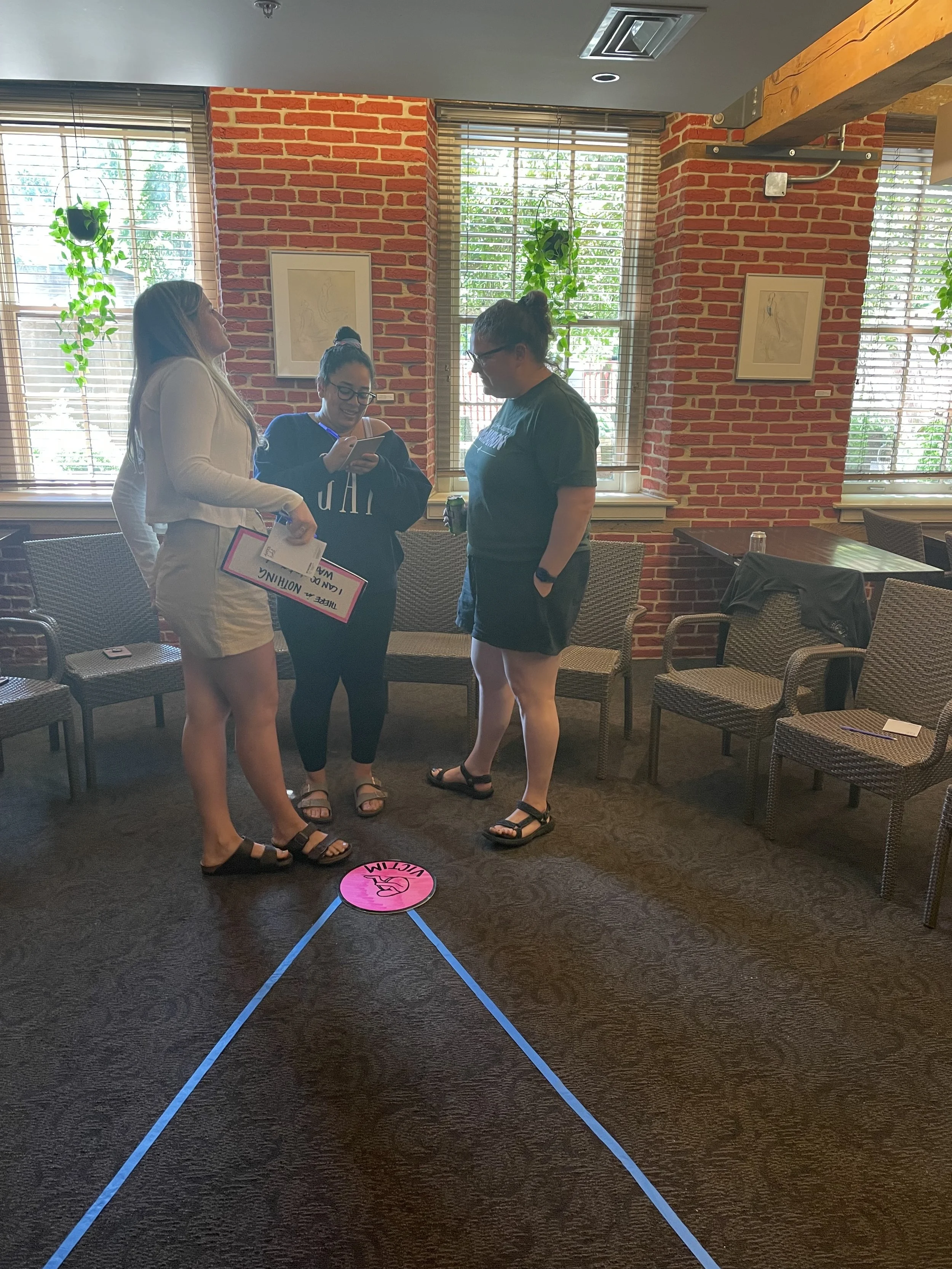 Participants stand at the tip of a blue tape triangle, participating in the Drama Triangle exercise.