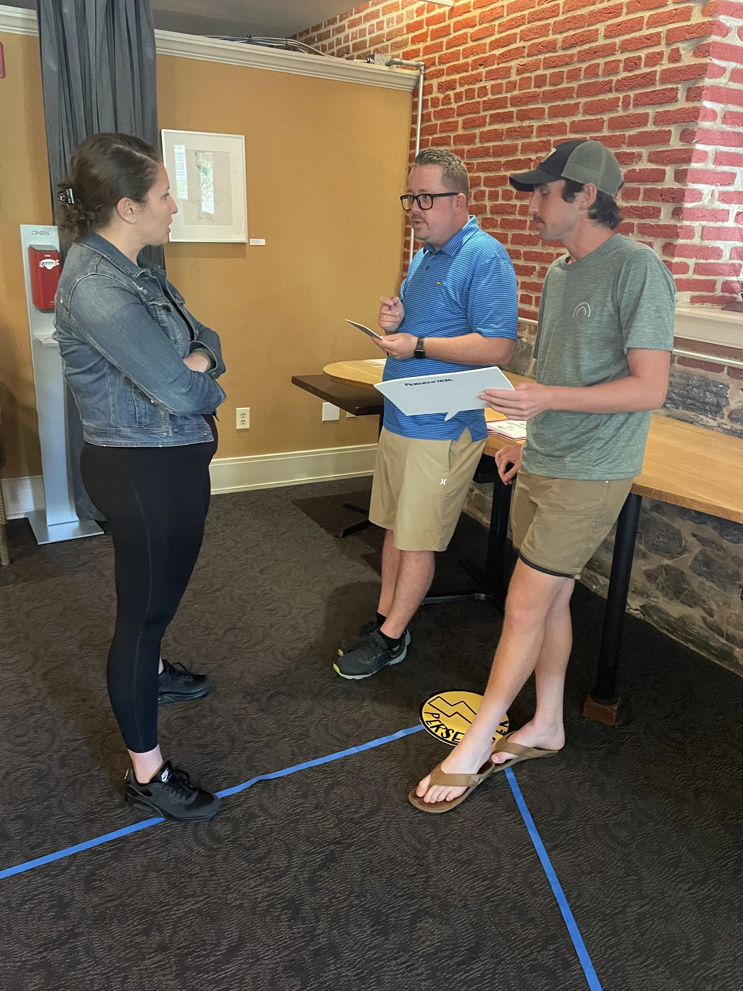 Participants stand at the tip of a blue tape triangle, participating in The Drama Triangle exercise.