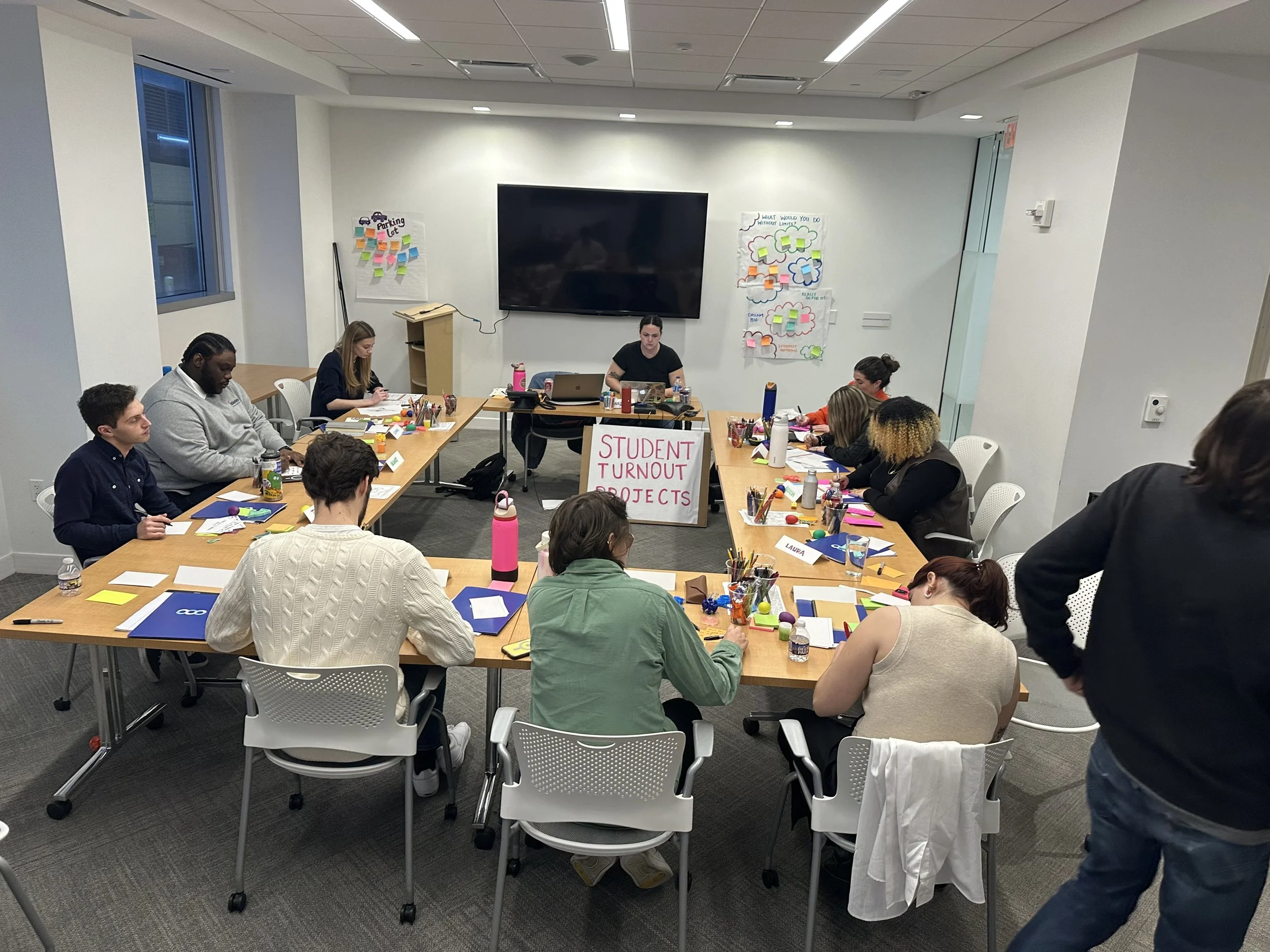 Kinship coach, Jules, facilitates a conversation with about 10 people around a U-shaped conference table in Washington, DC
