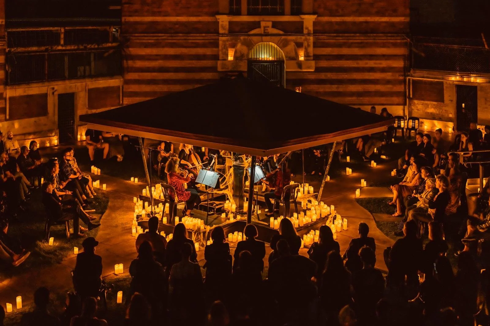 Photo of Paradiso Strings playing in concert surrounded by candlelight at Boggo Road Gaol