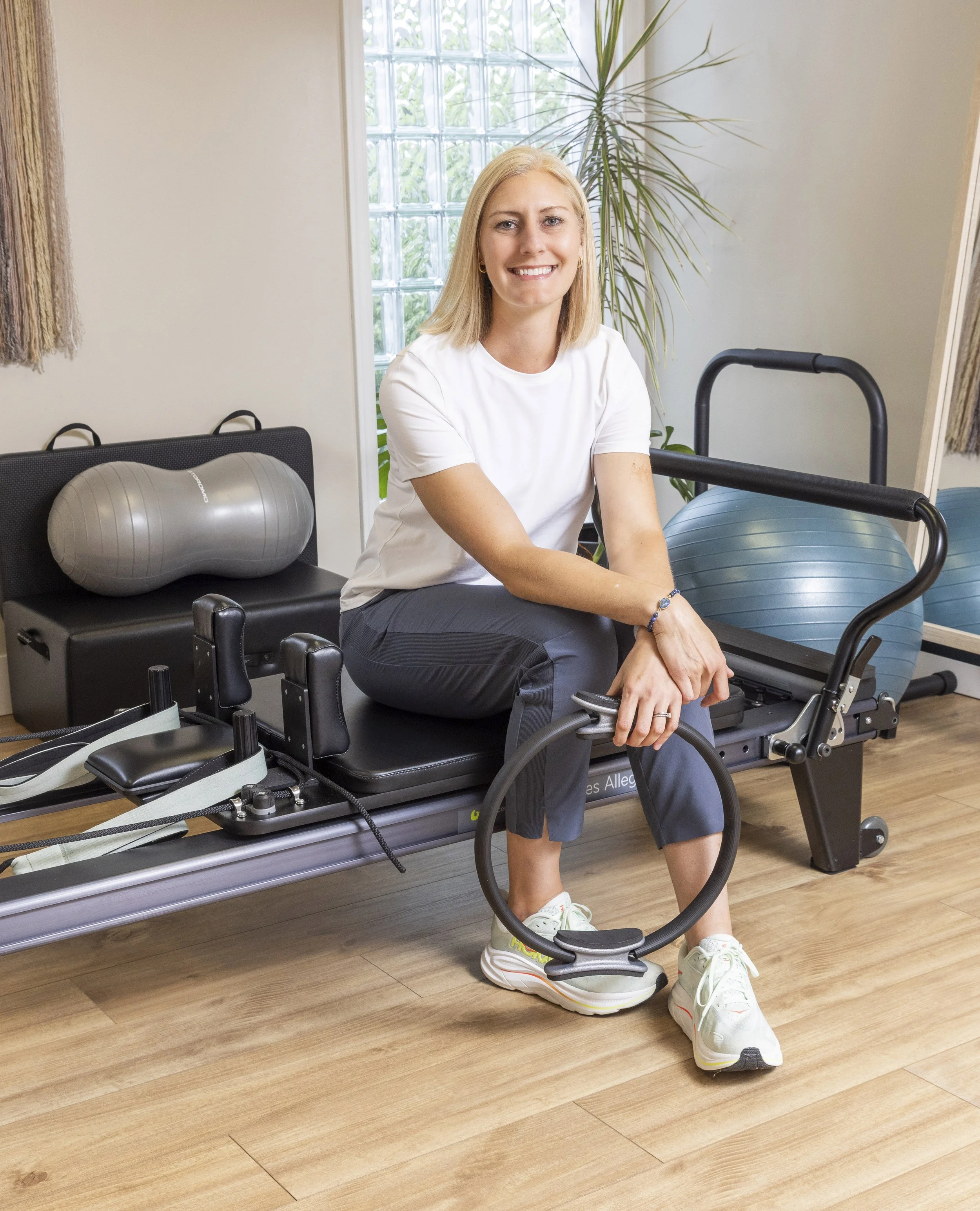  Blonde woman sitting on Balanced Body Allegro I Reformer holding a Magic Circle