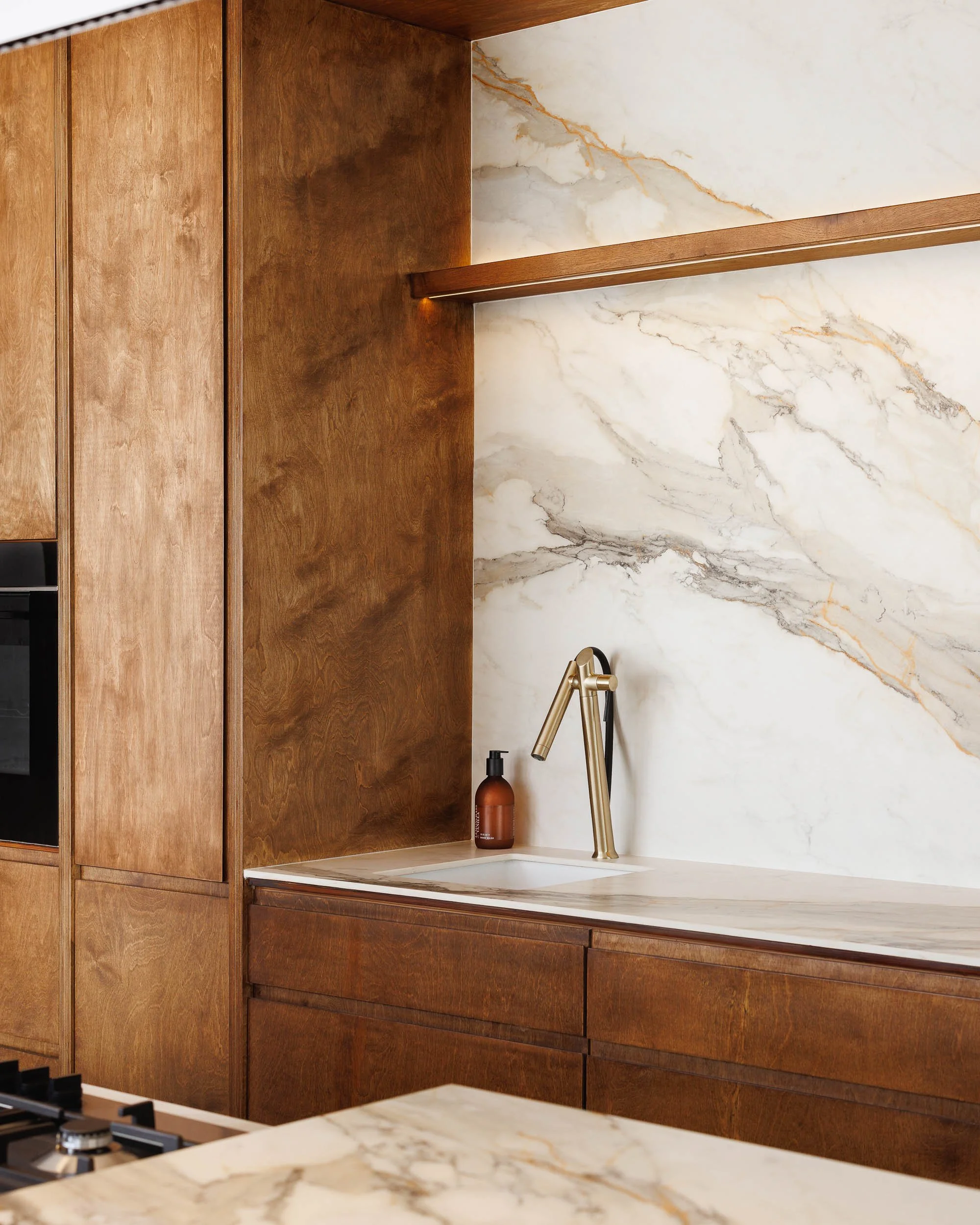 Kitchen sink nook with richly grained timber cabinetry, Calacatta marble splashback, and brushed brass tap