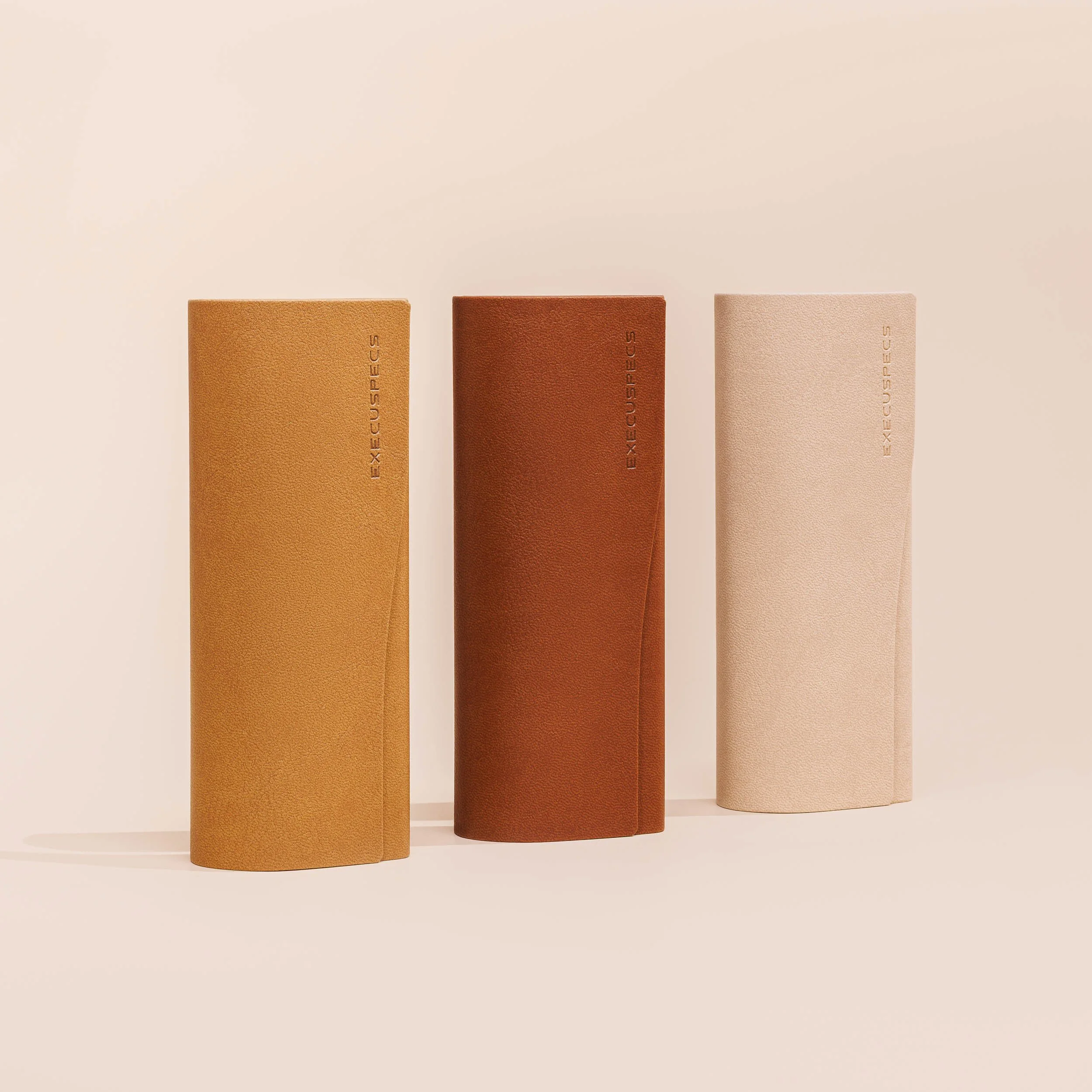 Three vertically standing cylindrical objects with textured surfaces in beige, rust, and a darker brown, each inscribed with the word 'EXCUSE' in light lettering, against a plain beige background.