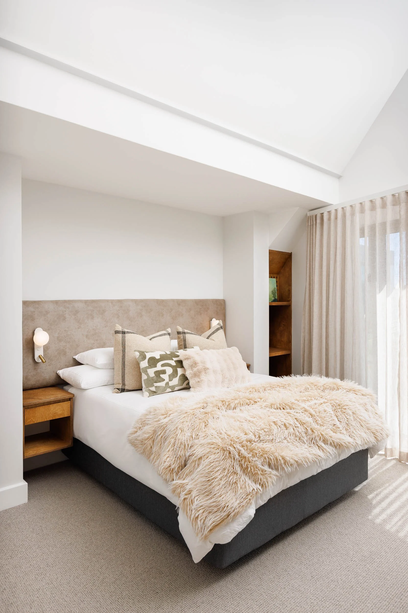 Guest bedroom with suede upholstered headboard, shearling throw, oak bedside tables, and linen drapes