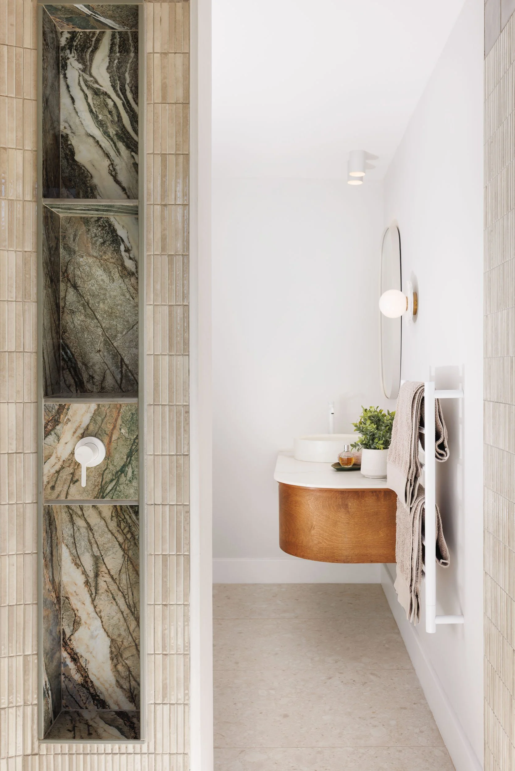 Bathroom with dramatic green-veined marble shower niches and curved timber floating vanity with round mirror