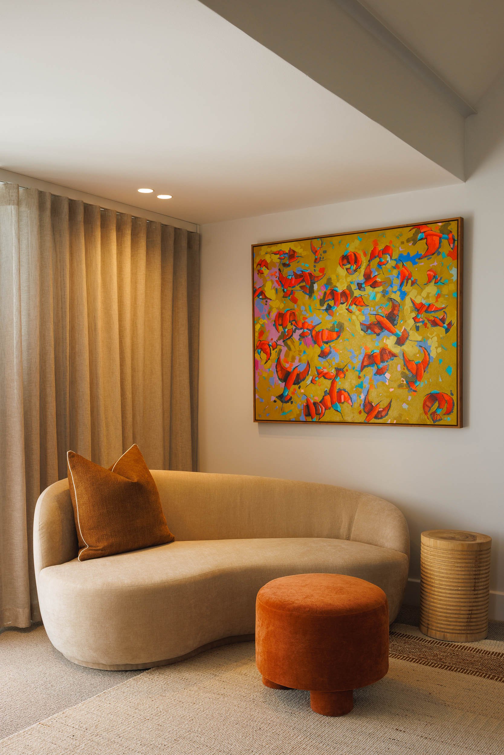 Sitting room corner with curved cream sofa, terracotta ottoman, and large abstract painting on gold ground