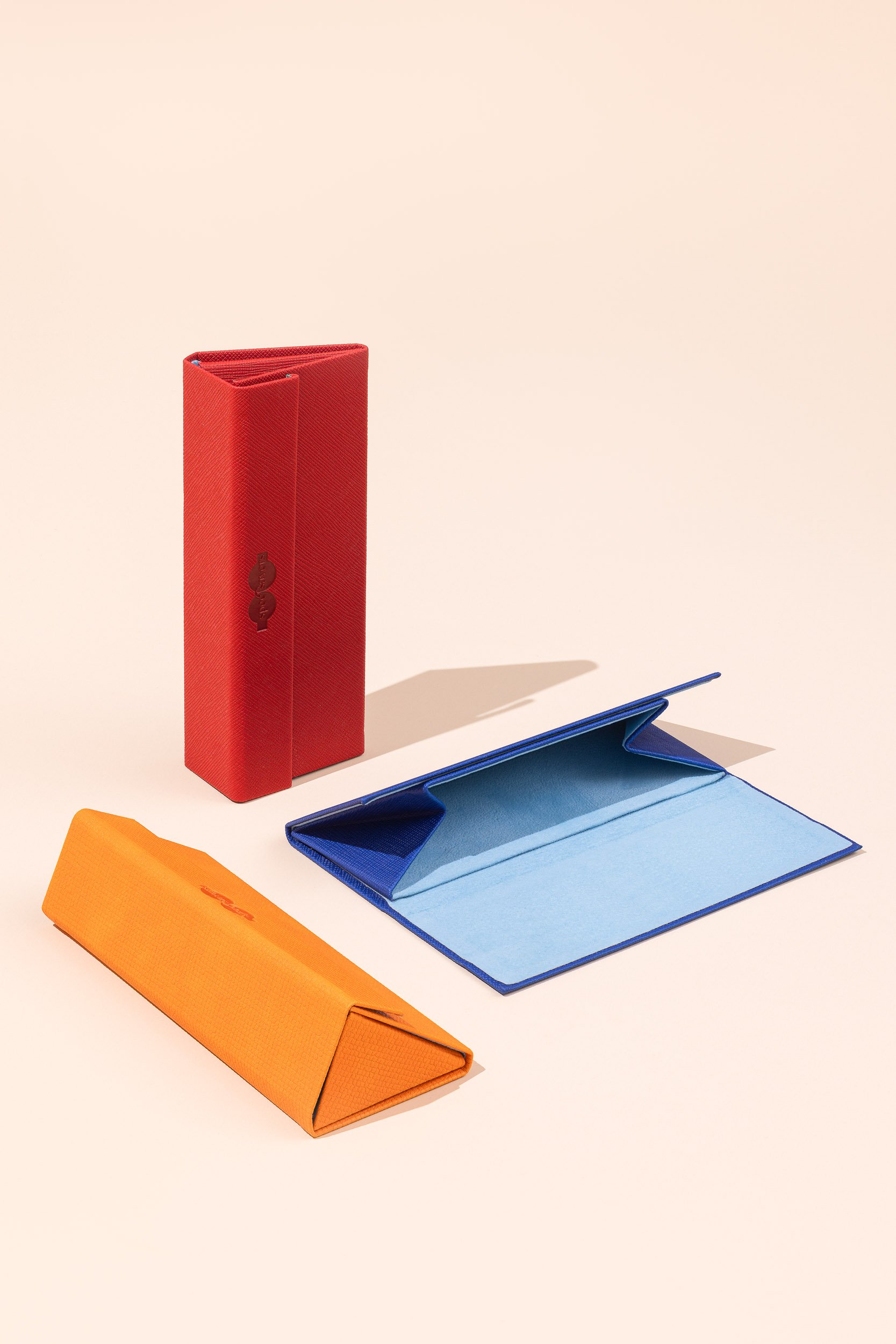 Colorful wallets and folders on a white background, including a red wallet standing upright, a blue folder laying open, and orange and yellow folded wallets.
